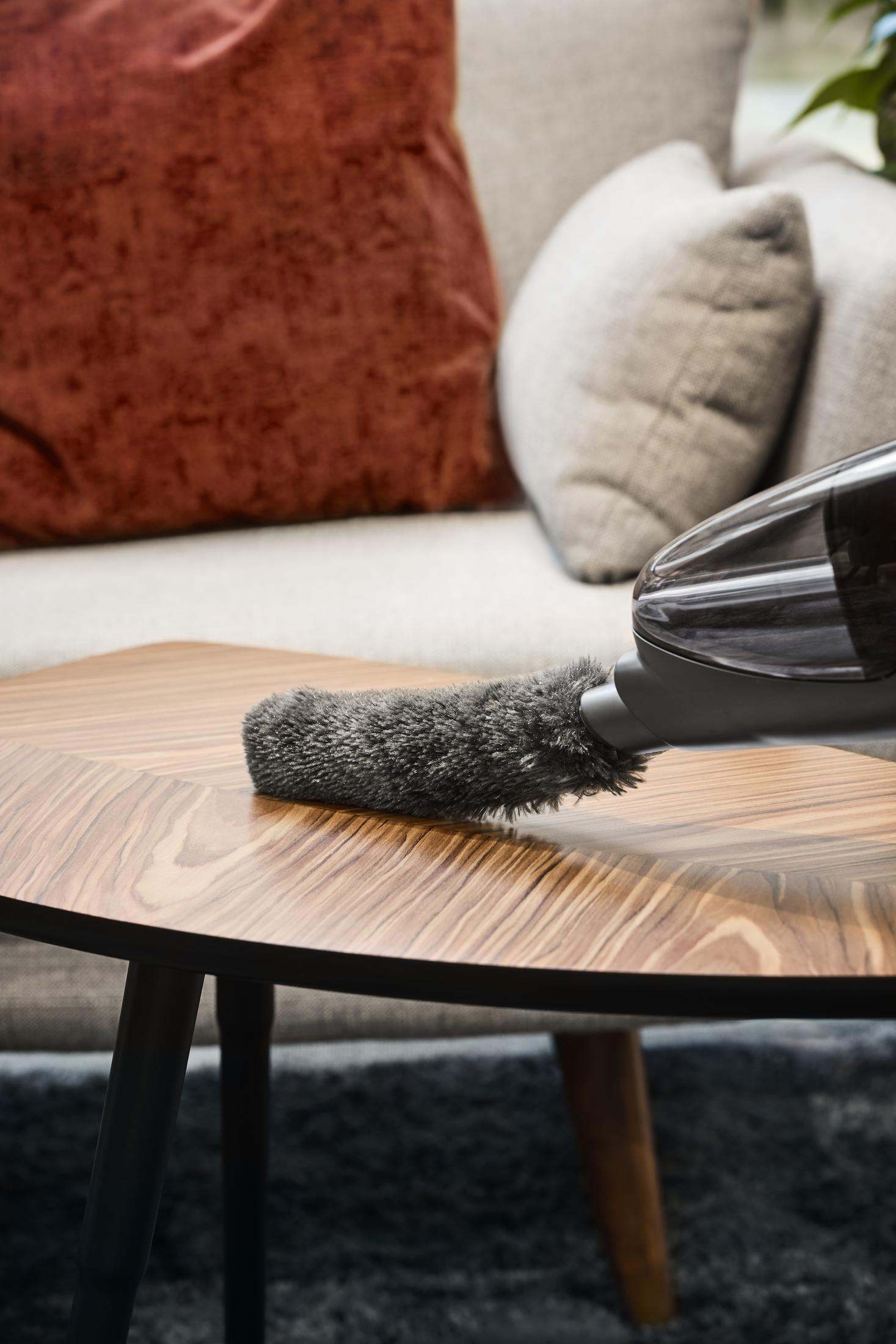 Głowica odkurzacza czyści drewniany stół. Szara szczotka dotyka stołu.