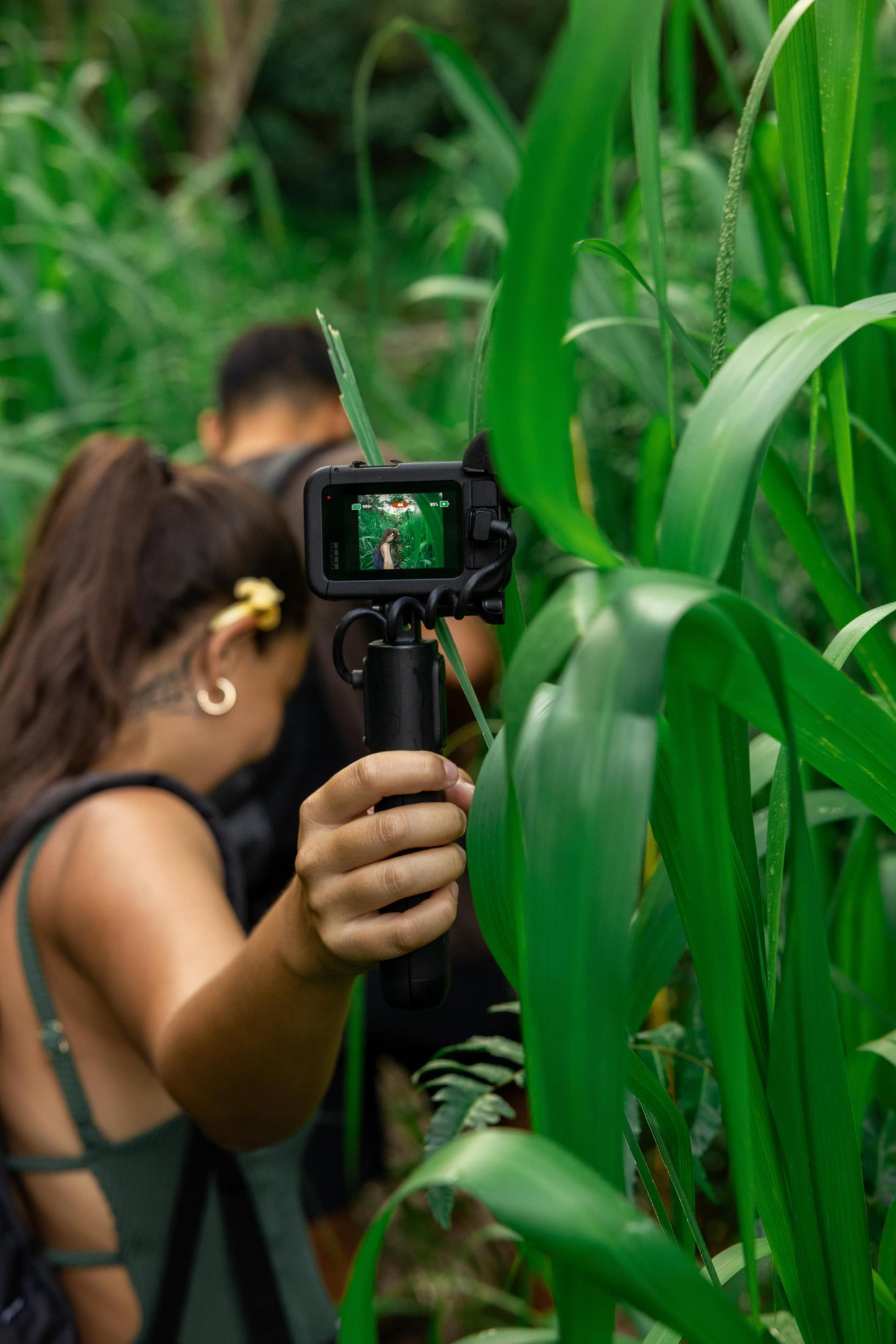 Osoba filmuje kamerą GoPro w wysokiej trawie. Druga osoba jest rozmyta w tle.