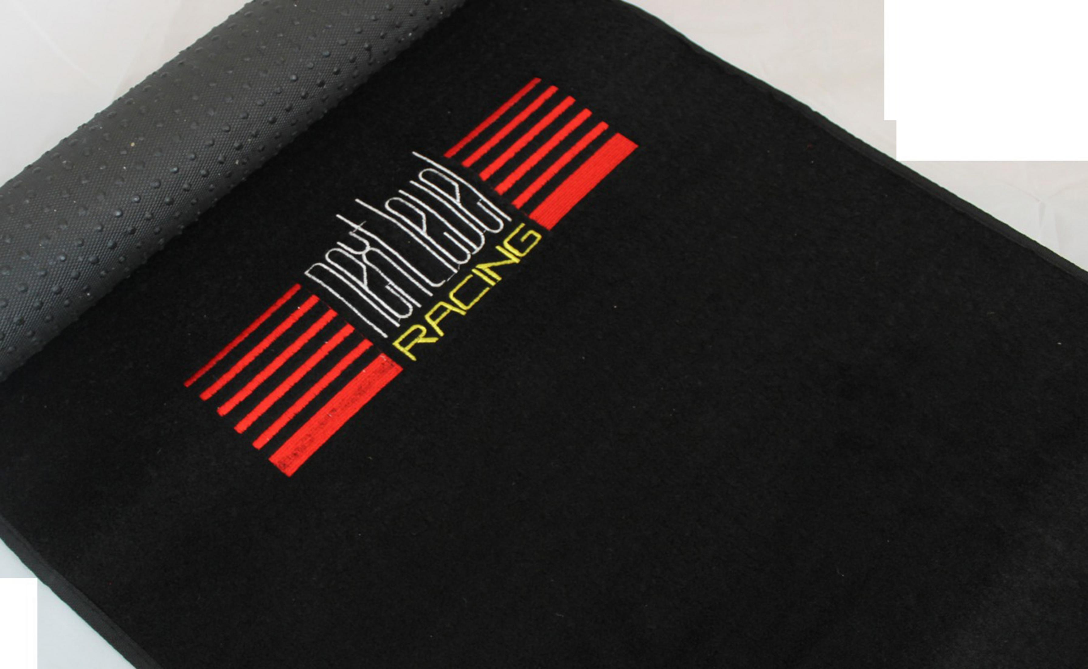 Schwarze Autoteppich mit roten Streifen und weißem Text 'RACING'. Der Teppich ist aufgerollt.