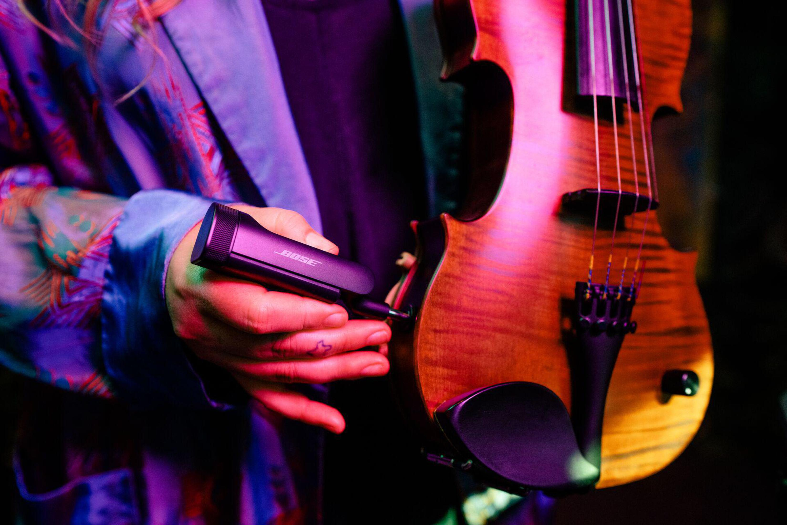 Una persona sosteniendo un dispositivo Bose negro junto a un violín.