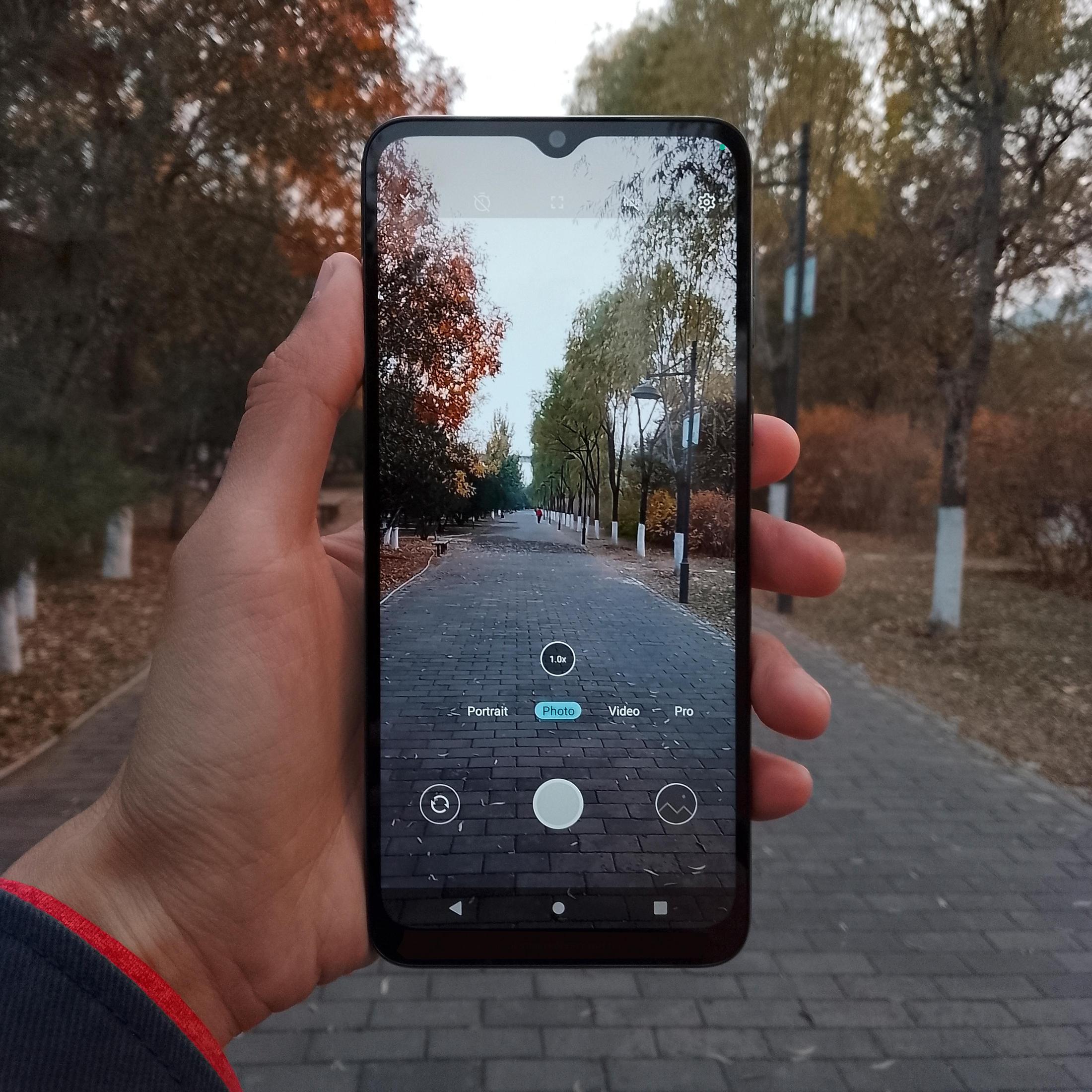 Dłoń trzymająca smartfona, robiąca zdjęcie ścieżki otoczonej drzewami.