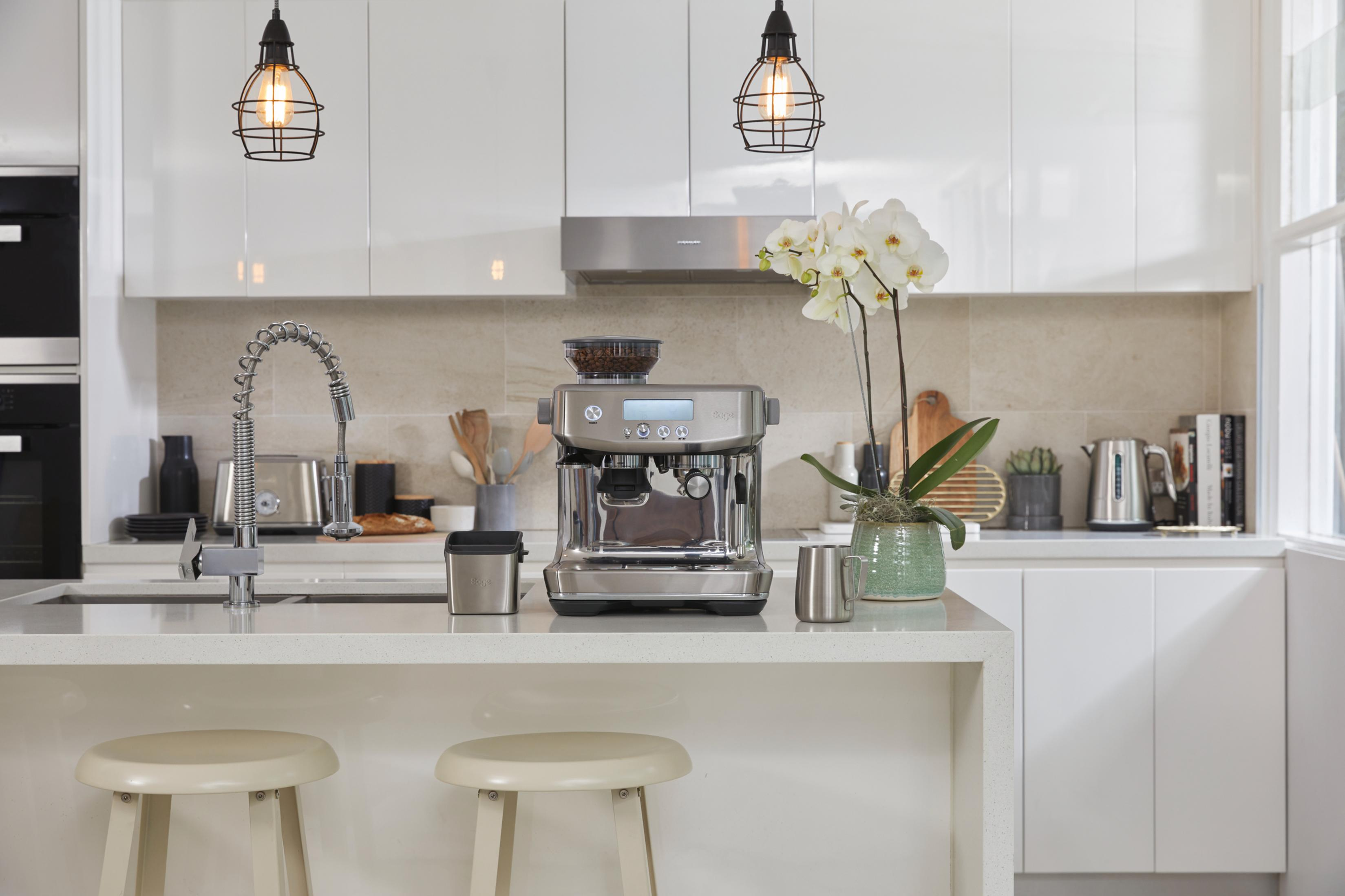 Küche mit weißen Schränken, Espressomaschine, heller Arbeitsplatte und zwei Pendelleuchten.