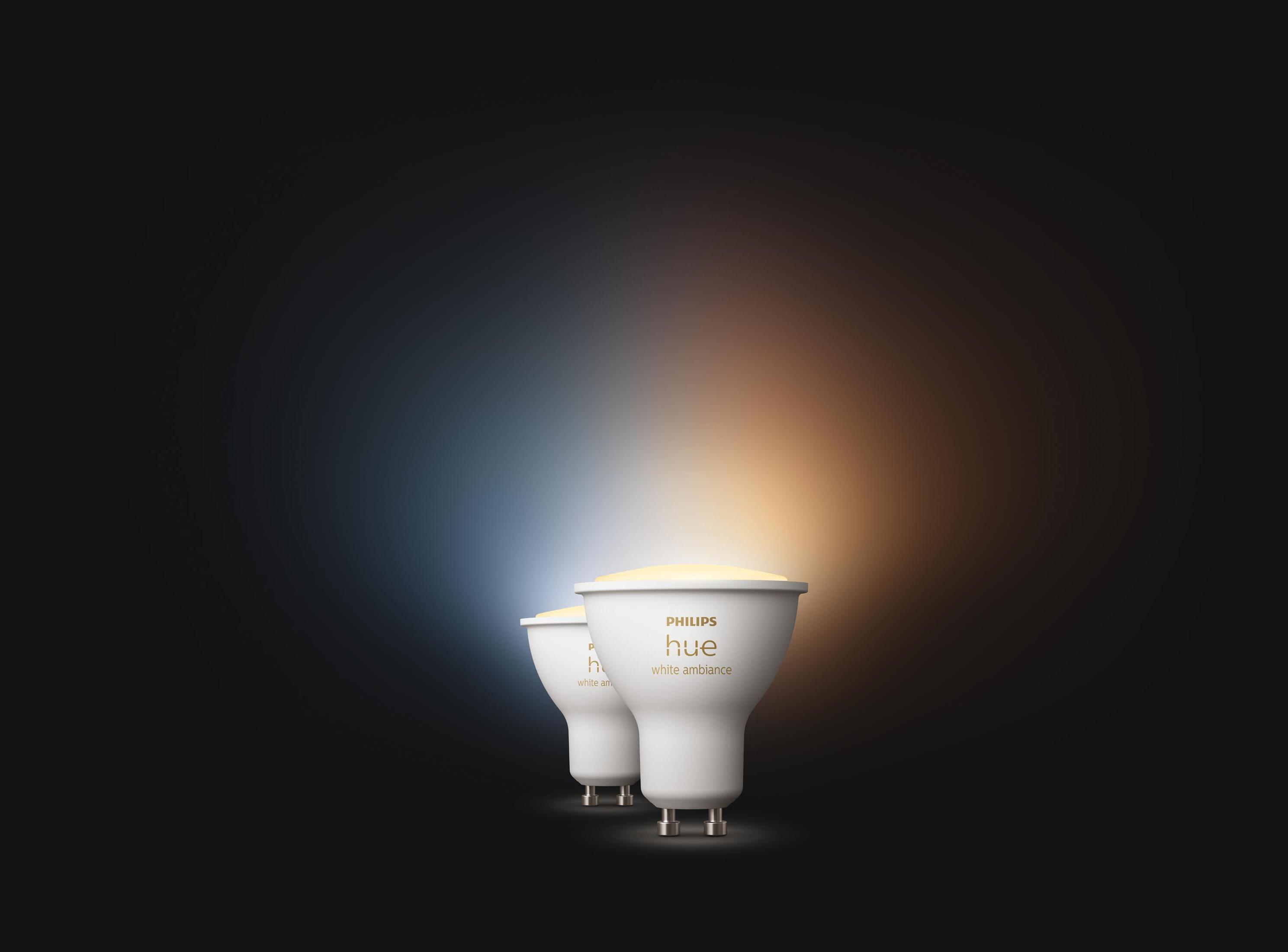 Dos bombillas inteligentes Philips Hue blancas sobre un fondo oscuro degradado, emitiendo luz cálida y fría.