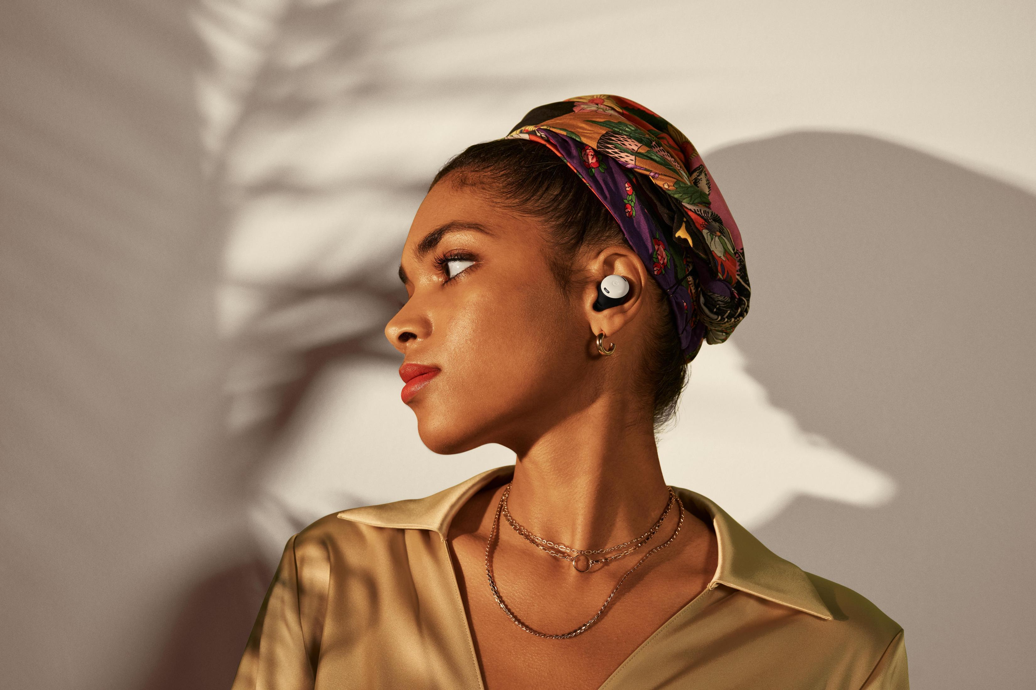 Kobieta ze słuchawkami i chustą na głowie patrzy w bok. Nosi złotą biżuterię i satynową koszulę.