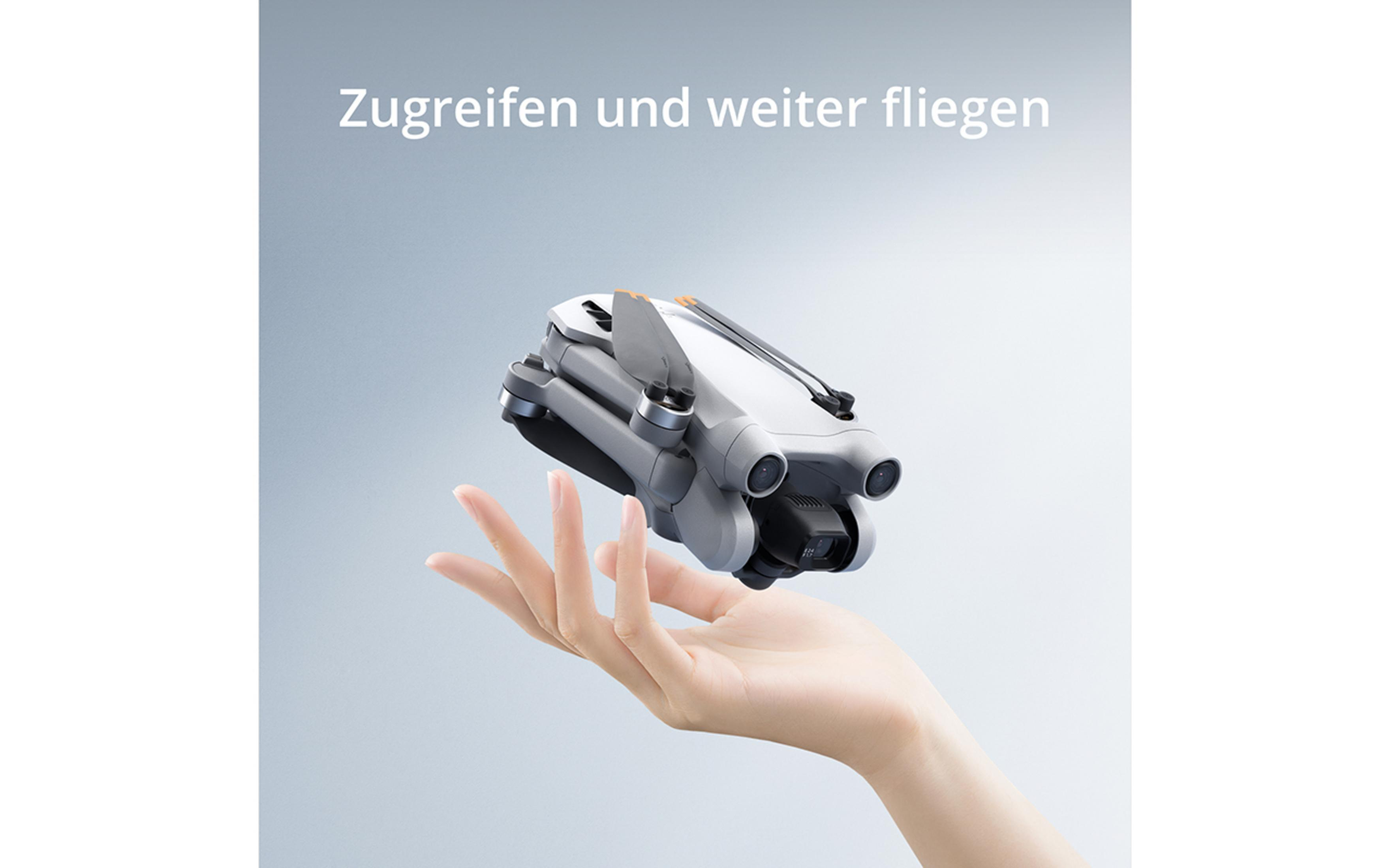 Hand hält eine graue Drohne. Drohne hat drei Kameras. Grauer Hintergrund und Text über der Drohne.