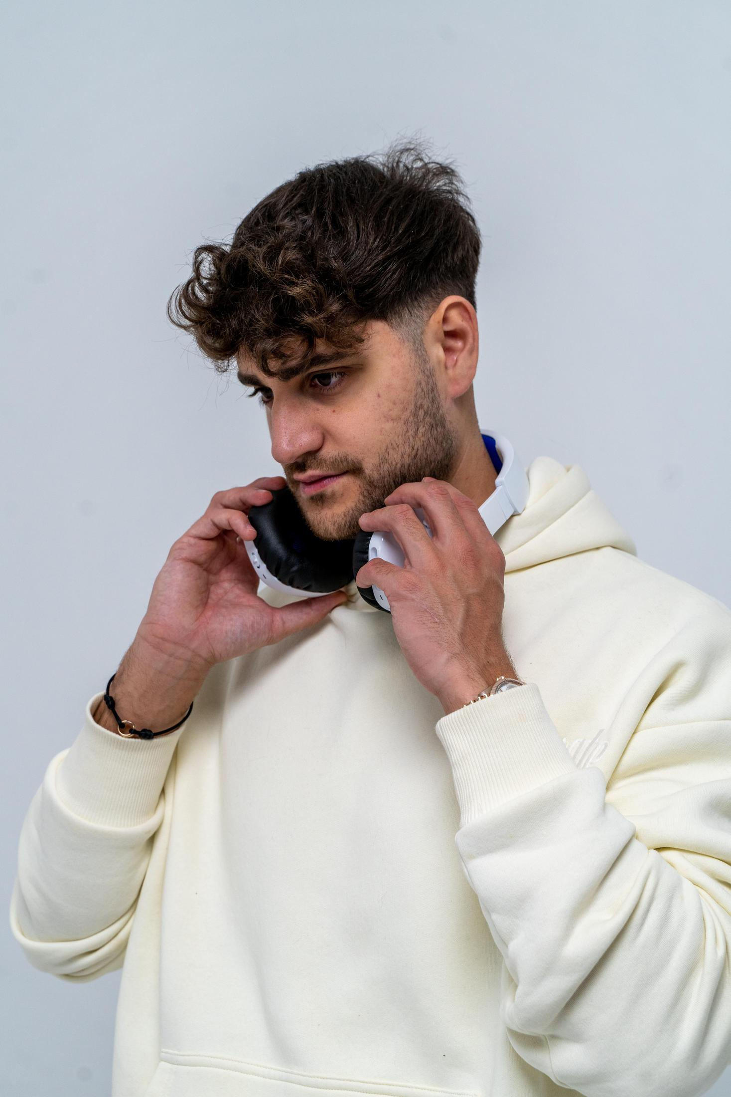 Mężczyzna ze słuchawkami na szyi, w białej bluzie z kapturem.