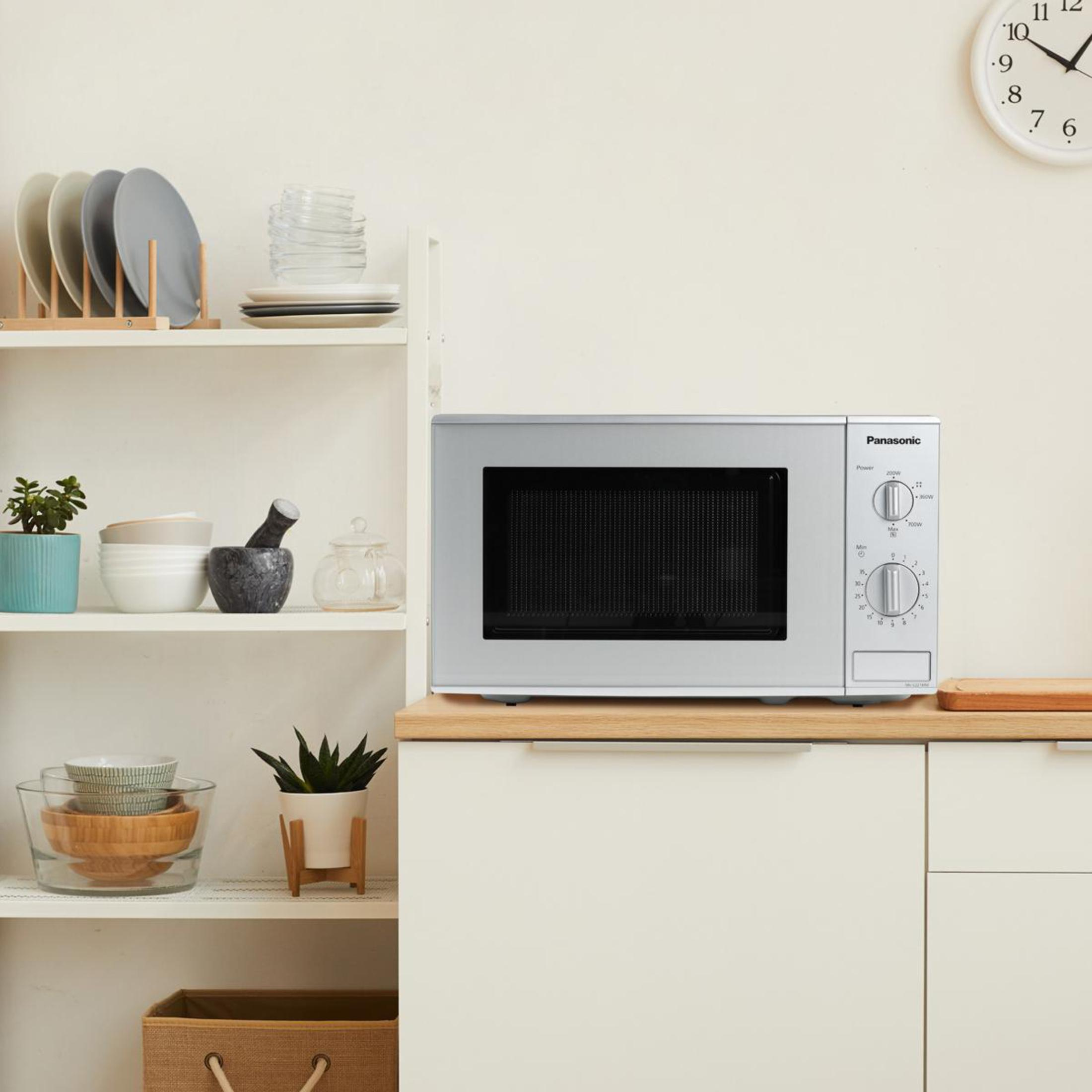 Srebrna kuchenka mikrofalowa Panasonic na białej szafce z półkami i dekoracjami.