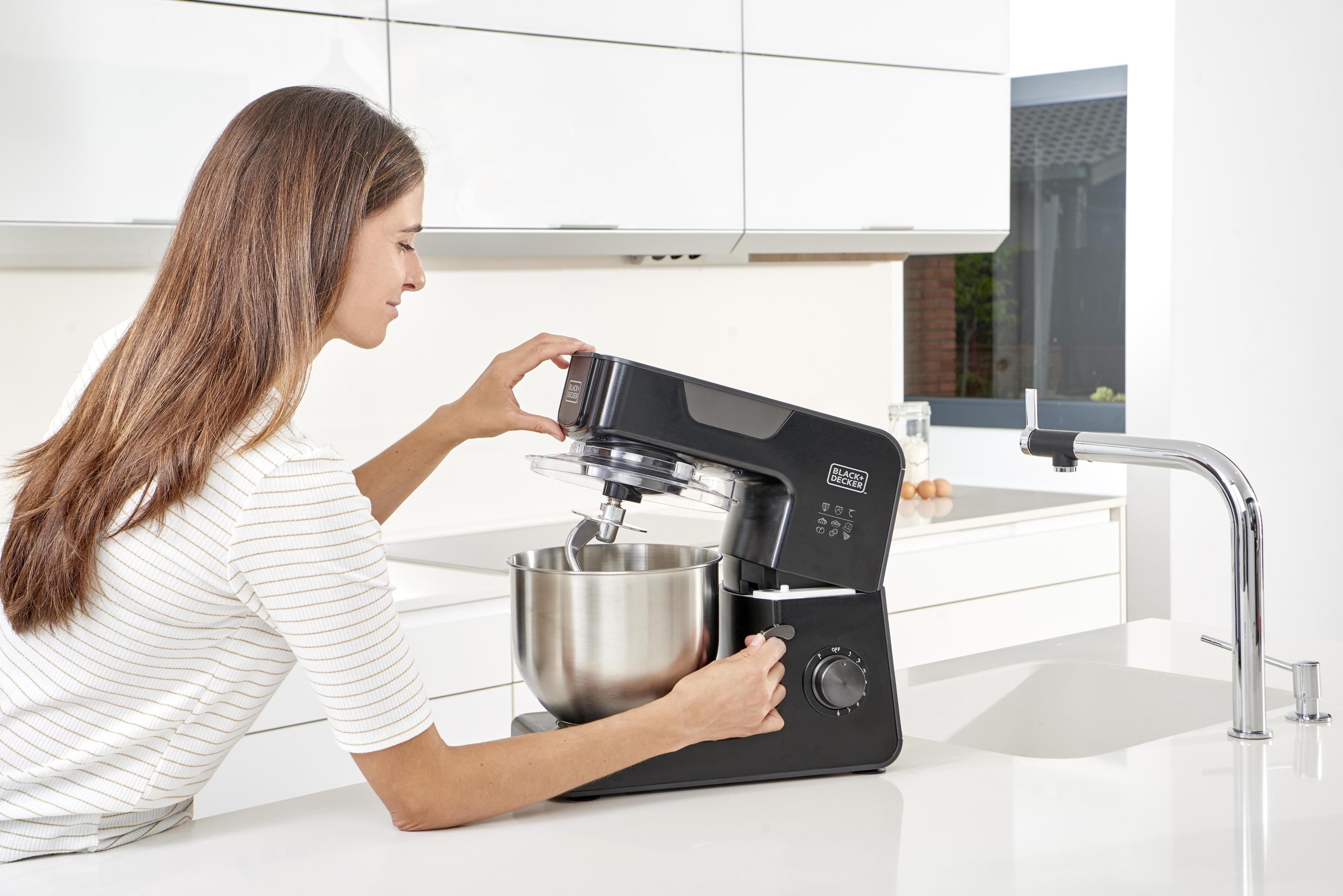 Frau benutzt eine schwarze Küchenmaschine in einer weißen Küche, Edelstahlschüssel.