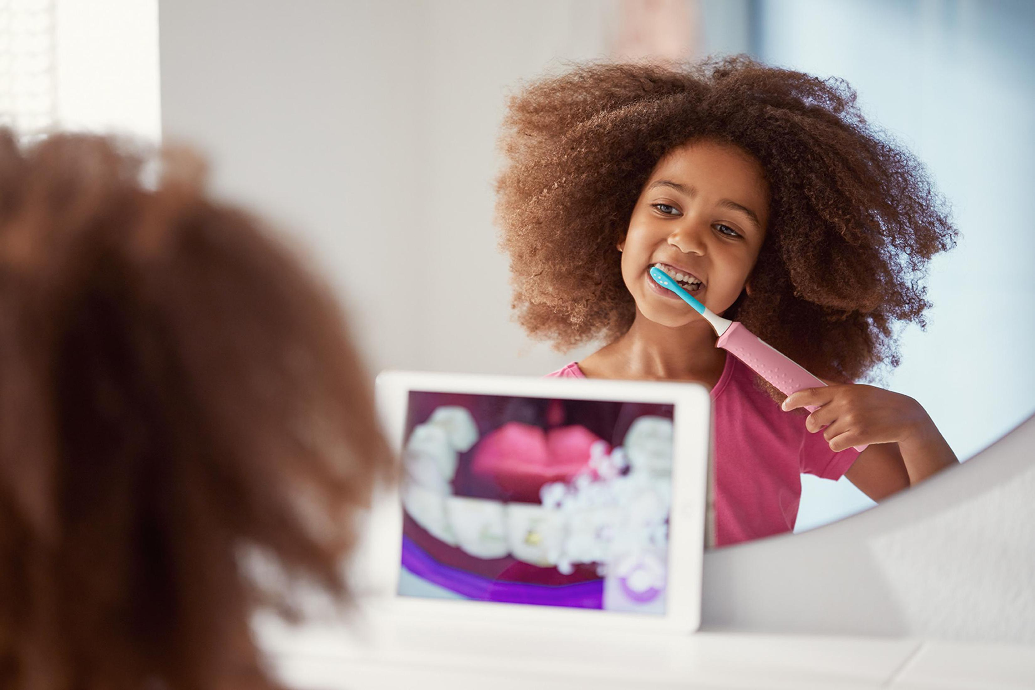 Una niña cepillándose los dientes mientras mira una pantalla que muestra una imagen dental.