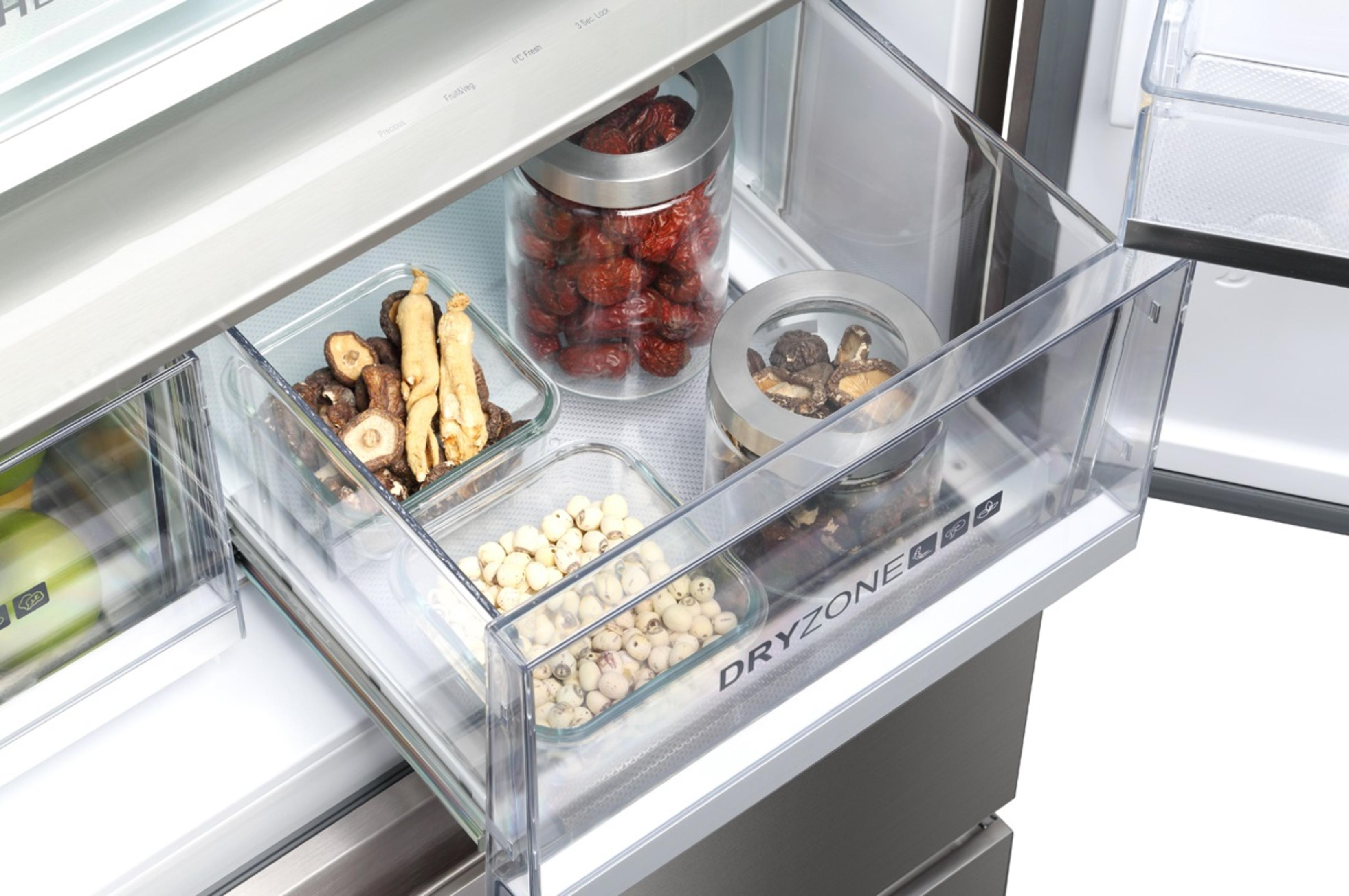 Cajón de refrigerador abierto lleno de recipientes de vidrio con alimentos.