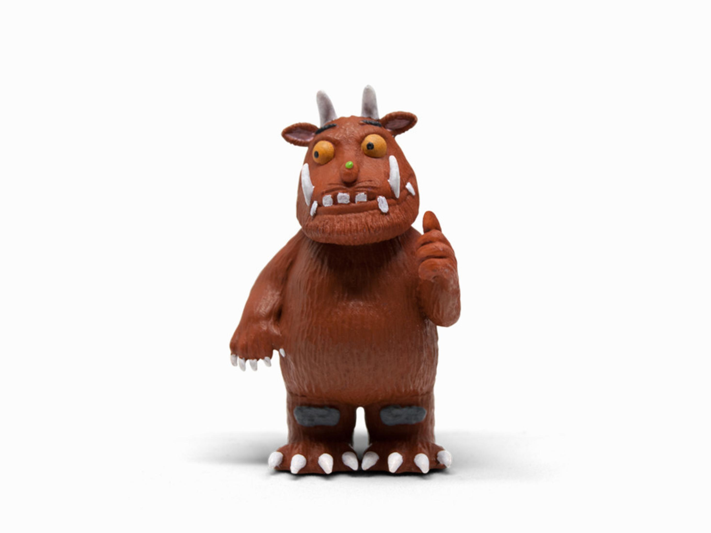 Ein braunes Gruffalo-Spielzeug mit Hörnern, Daumen hoch und weißen Zähnen, vor weißem Hintergrund.