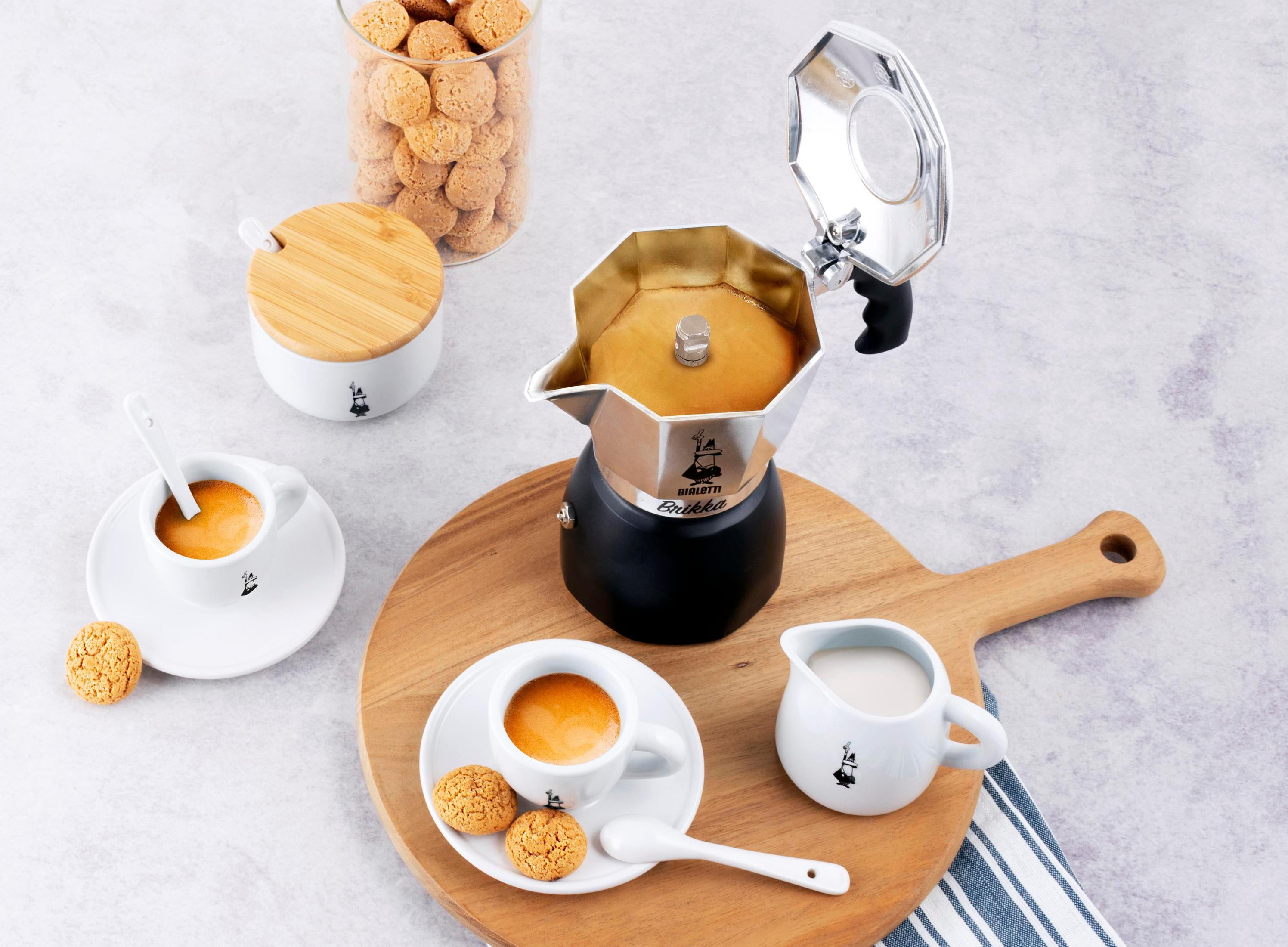 Ein Standbild eines Kaffee-Setups. Es enthält eine Kaffeemaschine, Tassen, Kekse und ein Holzbrett.