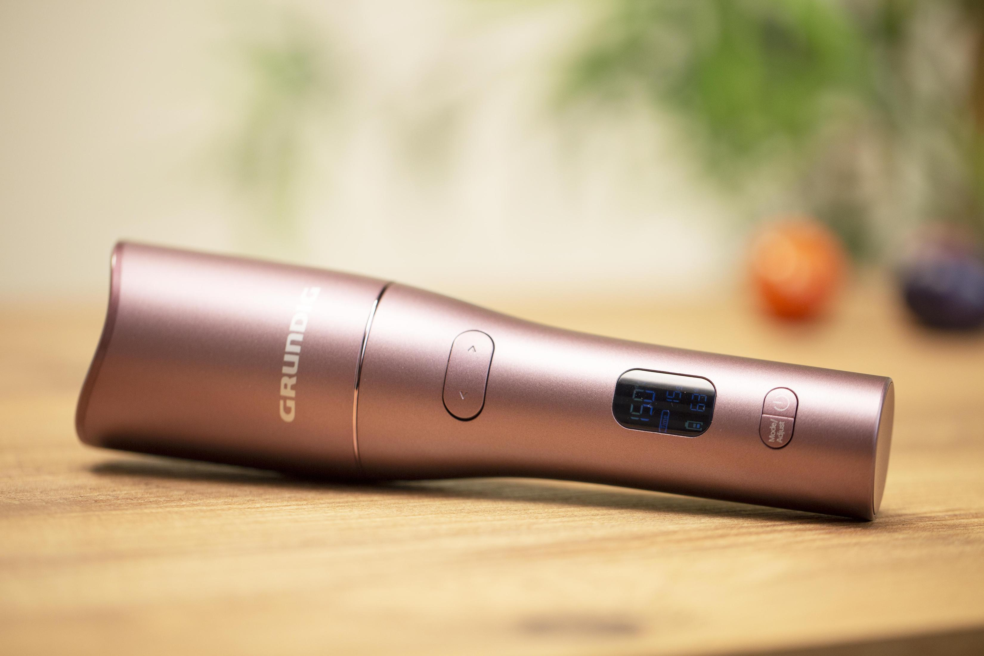 Un dispositivo Grundig color oro rosa è su un tavolo di legno, con un piccolo schermo e pulsanti.