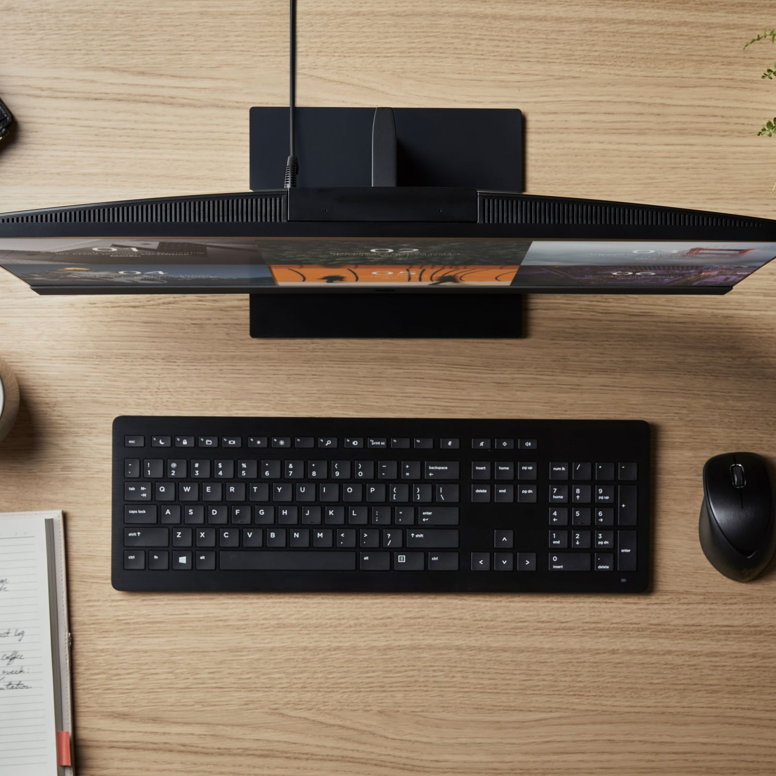 Widok z góry na czarny monitor, klawiaturę i mysz na drewnianym biurku.