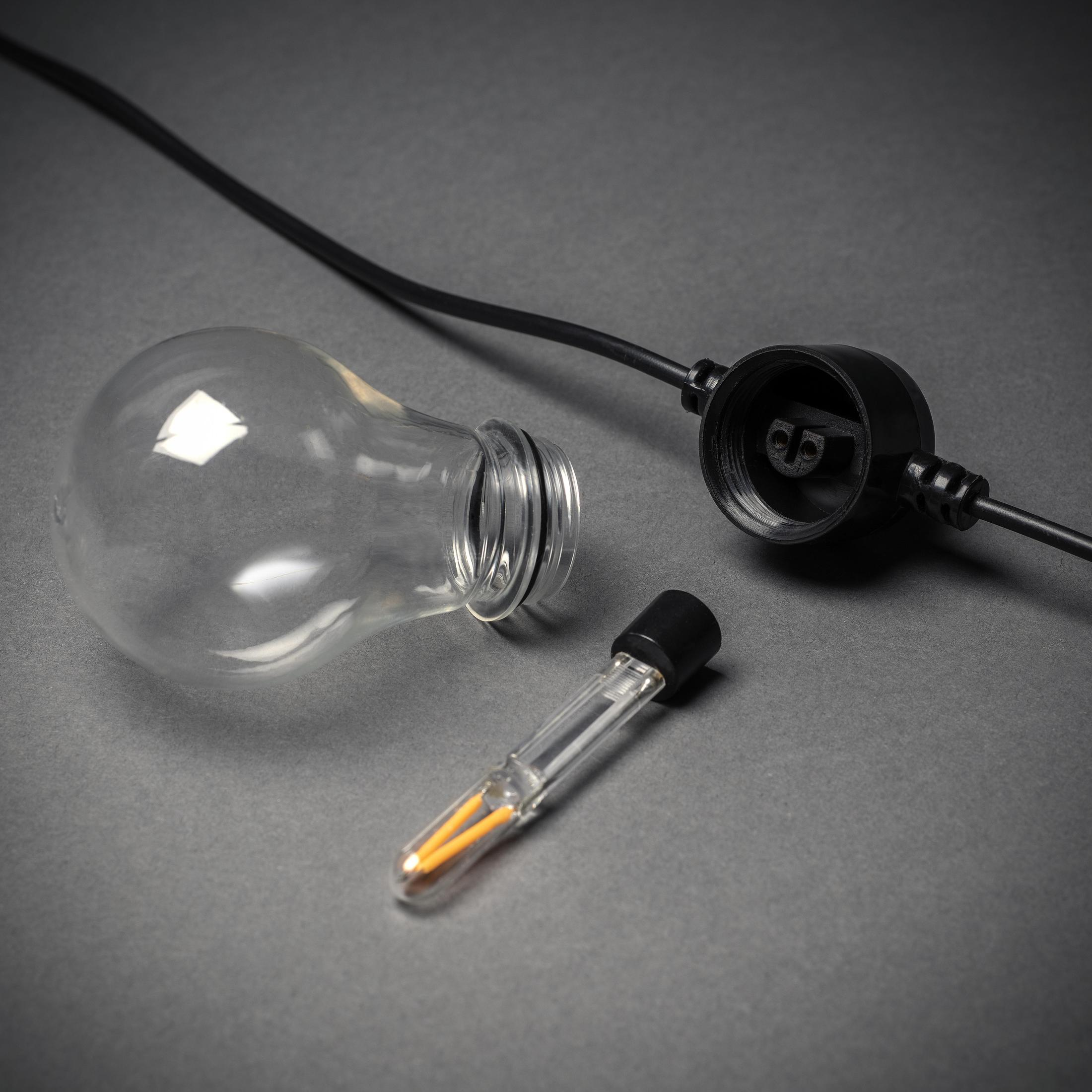 Eine unbeleuchtete Glühbirne, ein Stecker und eine kleine Birne mit zwei Filamenten auf grauem Untergrund.