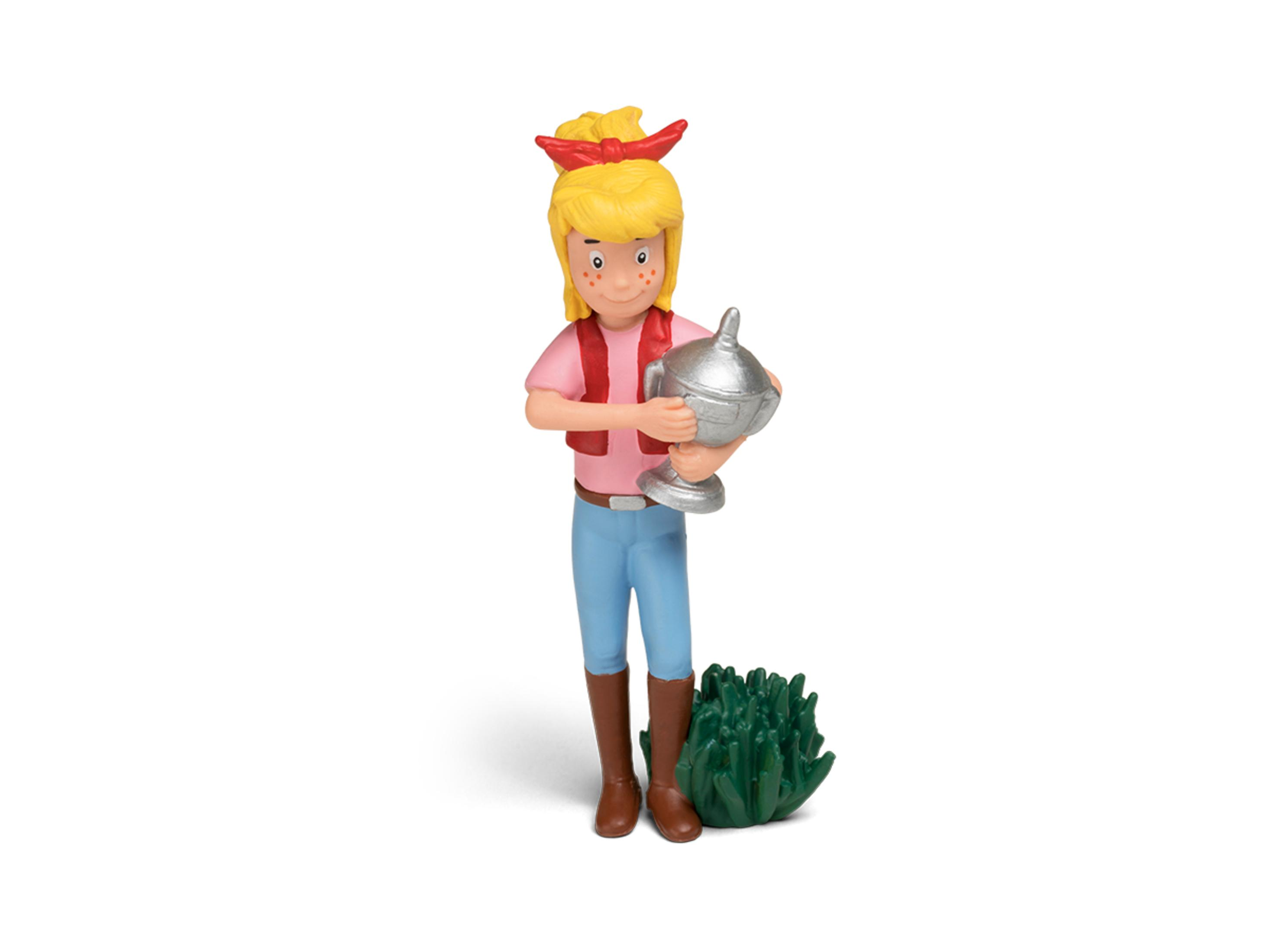 Eine Mädchenfigur mit einer Trophäe. Sie trägt ein rosa Hemd, blaue Hose und braune Stiefel. Grüner Busch.