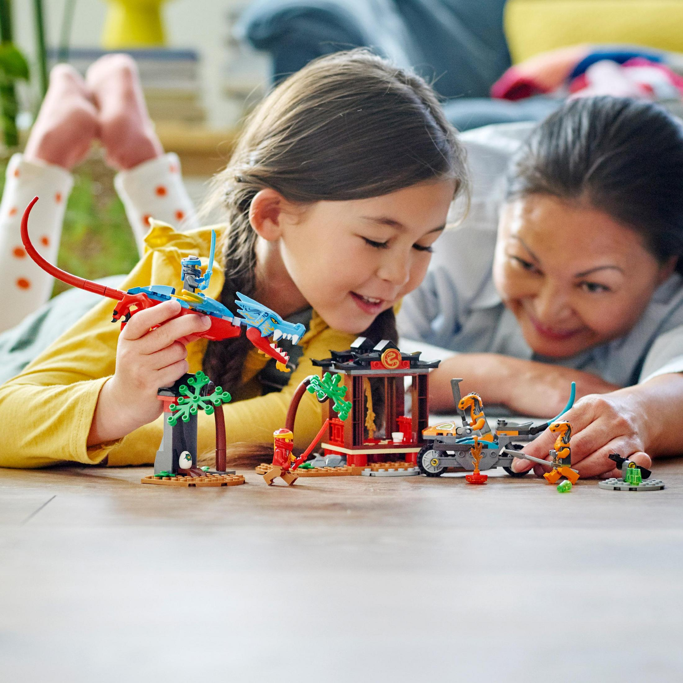 Zwei Personen spielen mit einem Lego-Set mit Drachen und Figuren.