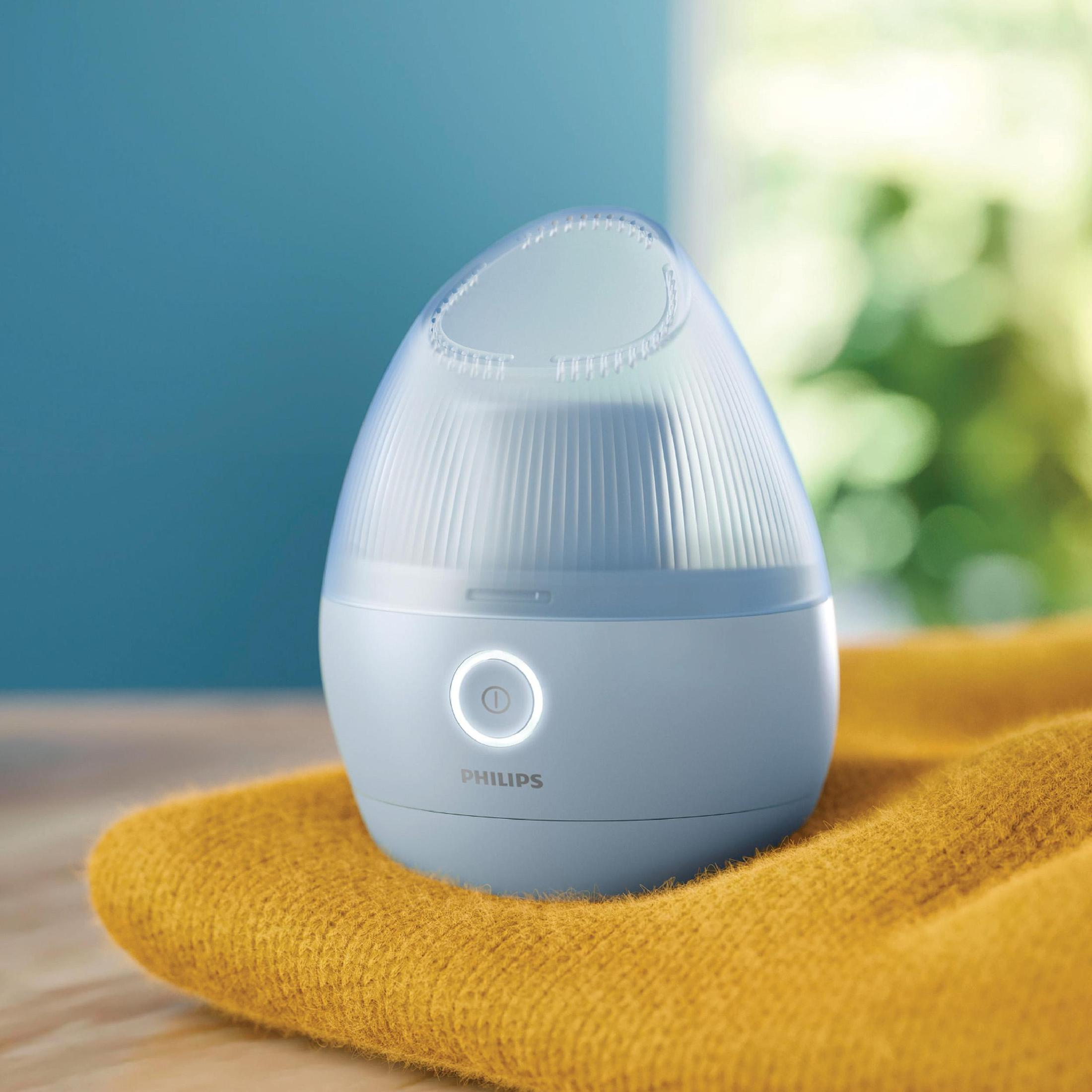 Sarı havlu üzerinde, yumuşak mavi bir arka plan önünde, açık mavi bir Philips yüz buhar makinesi.