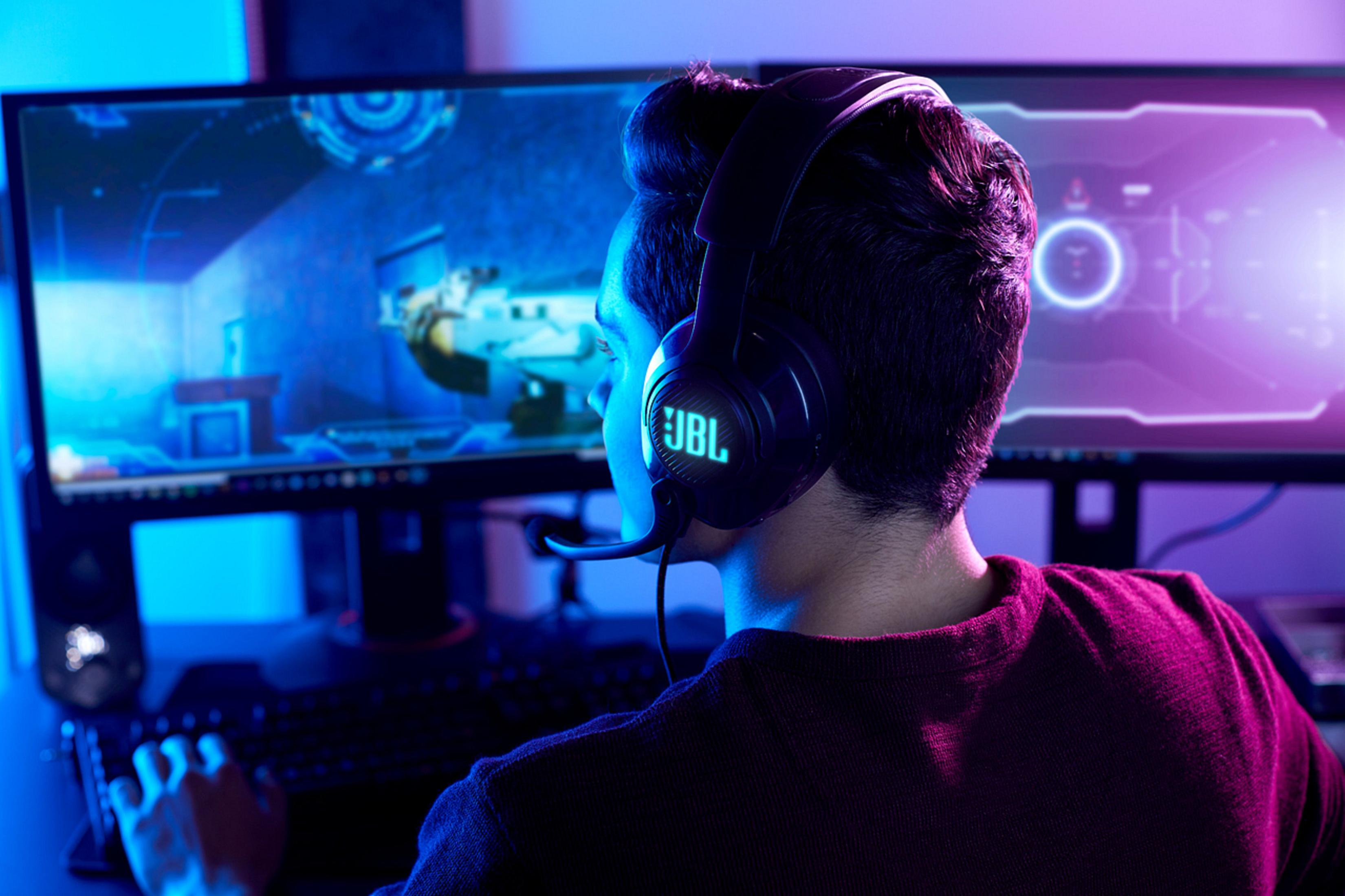 Una persona usando auriculares JBL mientras juega un videojuego en un monitor.