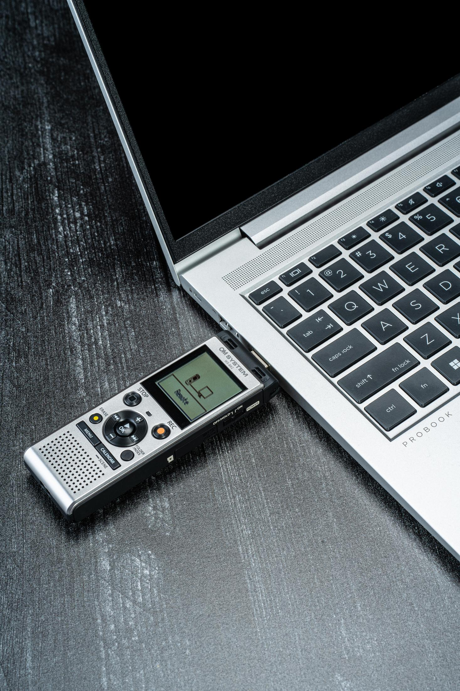 Cyfrowy rejestrator głosu jest podłączony do laptopa na ciemnej powierzchni.