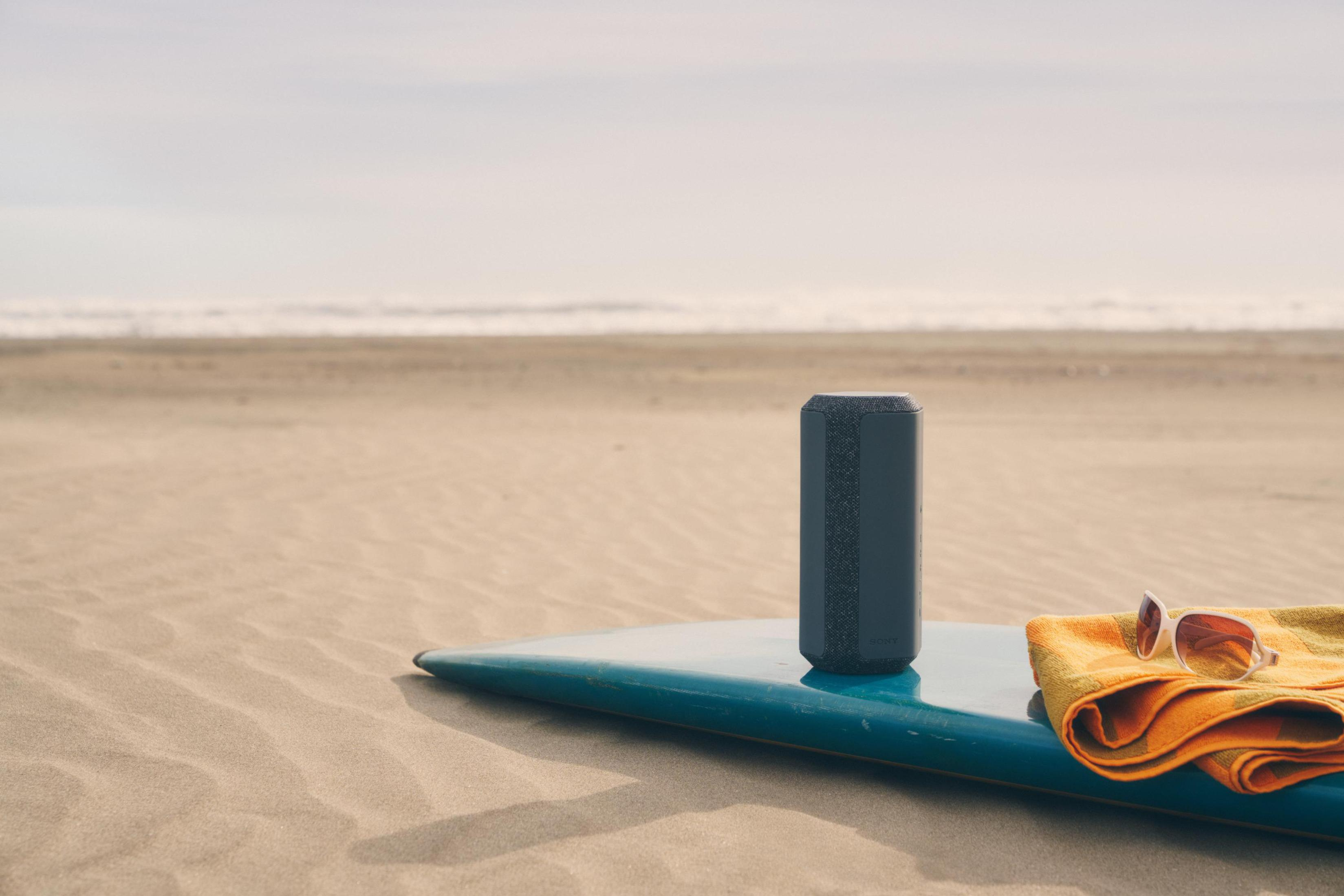 Strandszene mit Lautsprecher, Sonnenbrille und Handtuch auf Surfbrett.
