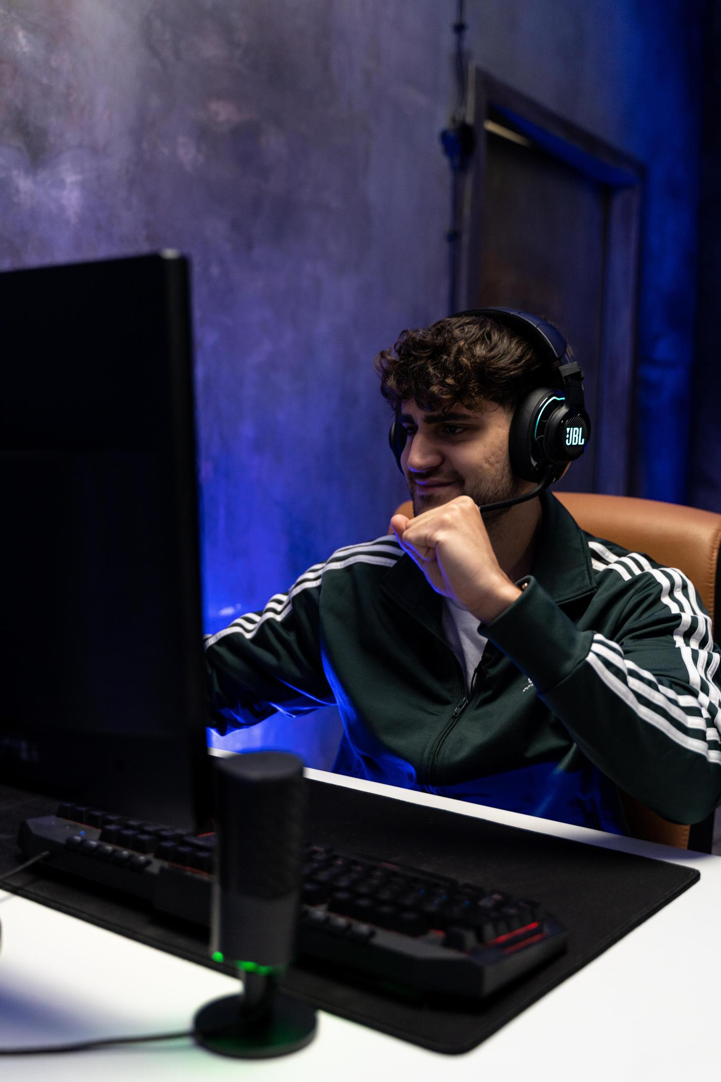 Mężczyzna w słuchawkach i zielonej kurtce, patrzący na ekran komputera podczas grania.