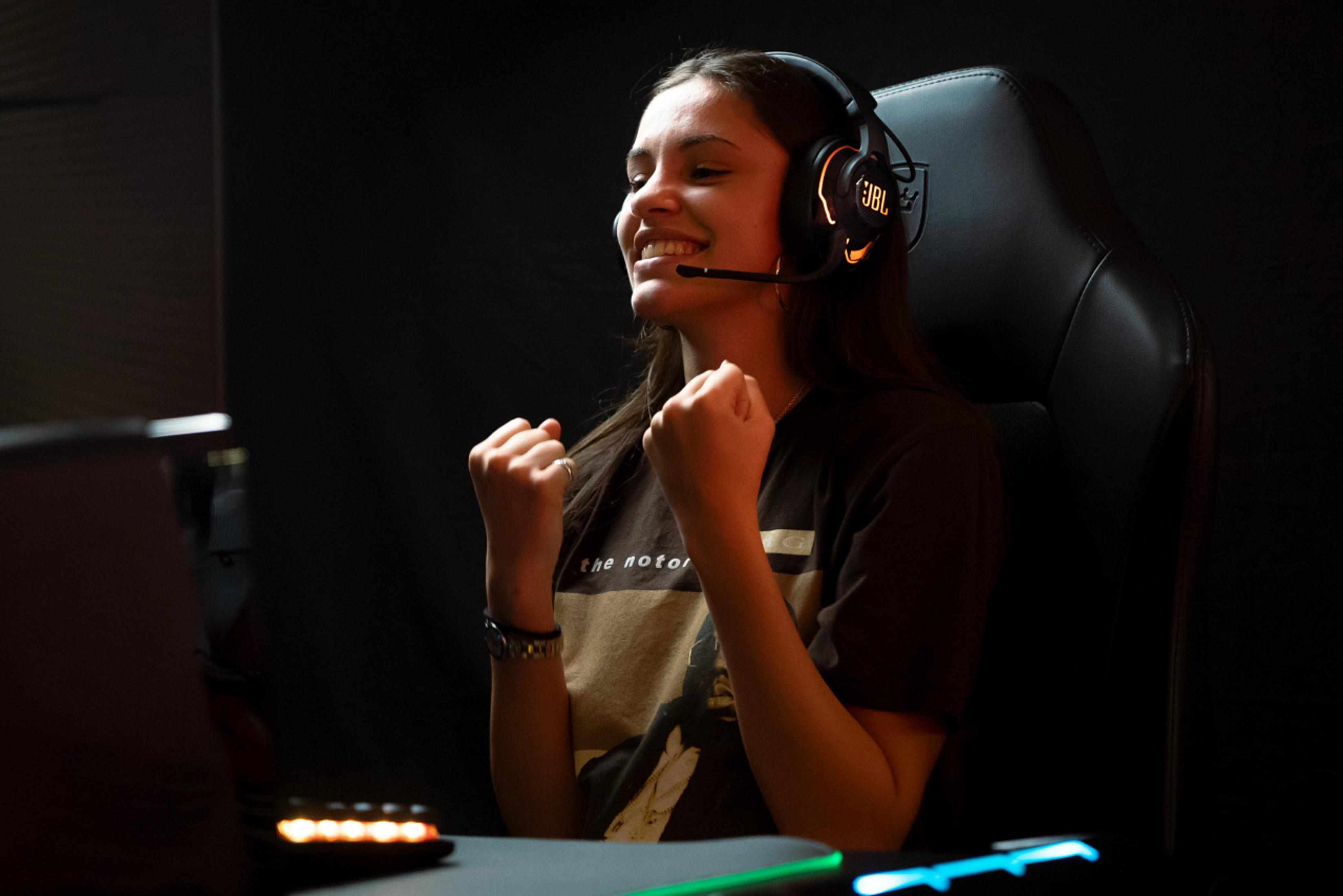 Młoda kobieta w słuchawkach, uśmiechnięta i świętująca, grająca.