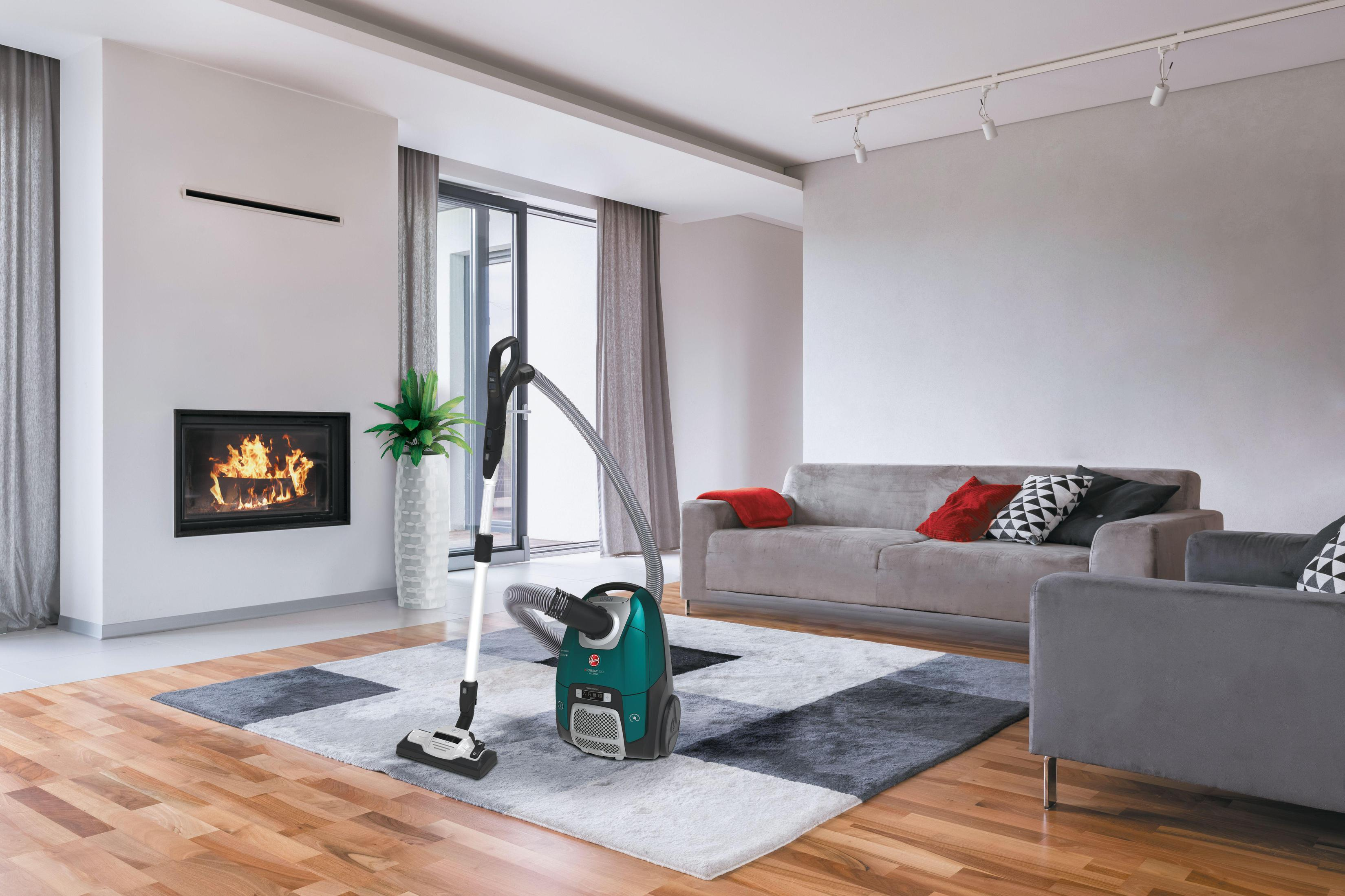 Salon z odkurzaczem, kominkiem, sofą i krzesłami. Podłoga z twardego drewna i dywan.