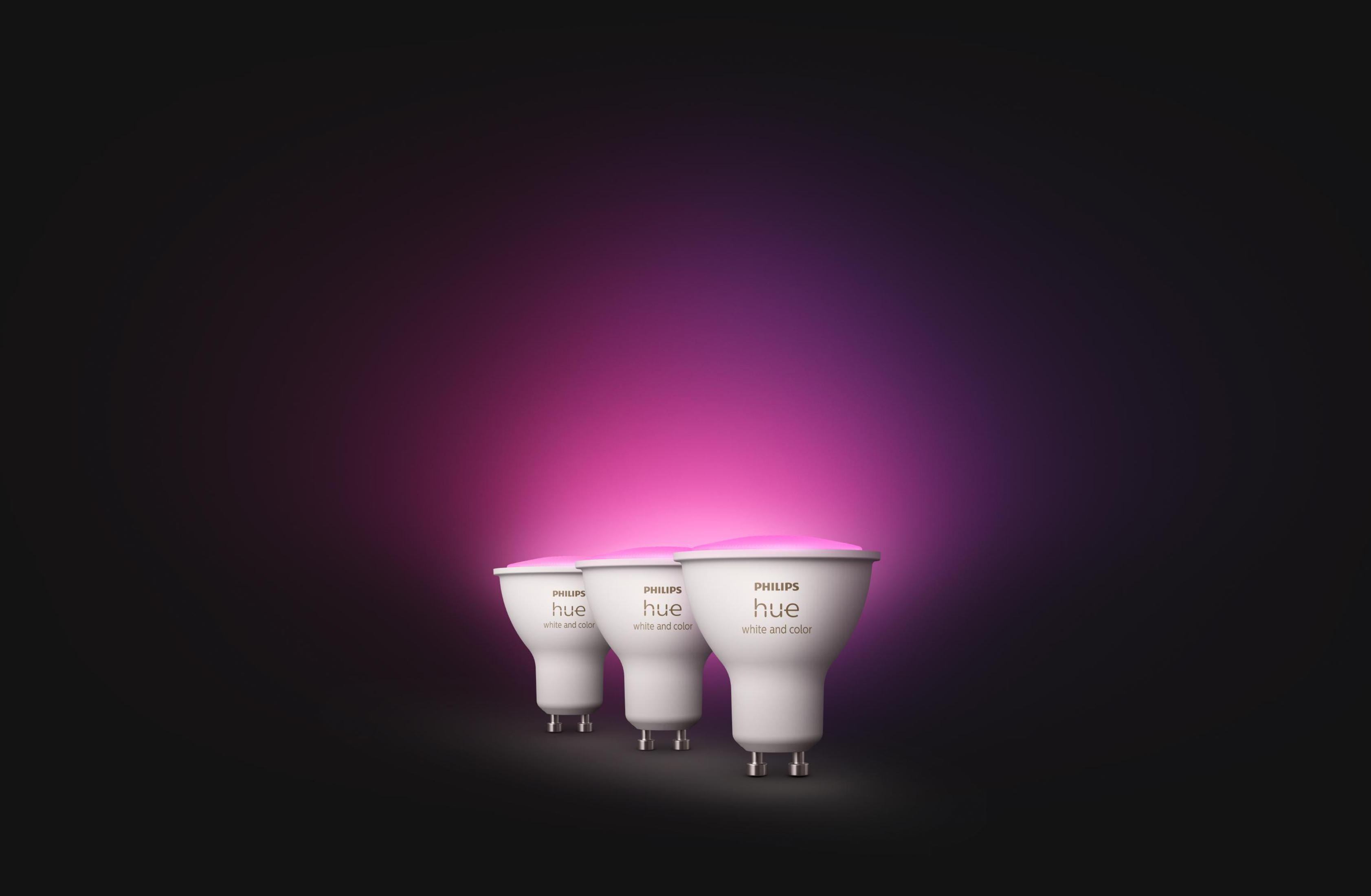 Drei weiße Philips Hue-Glühbirnen, die rosa Licht ausstrahlen, auf dunklem Hintergrund.
