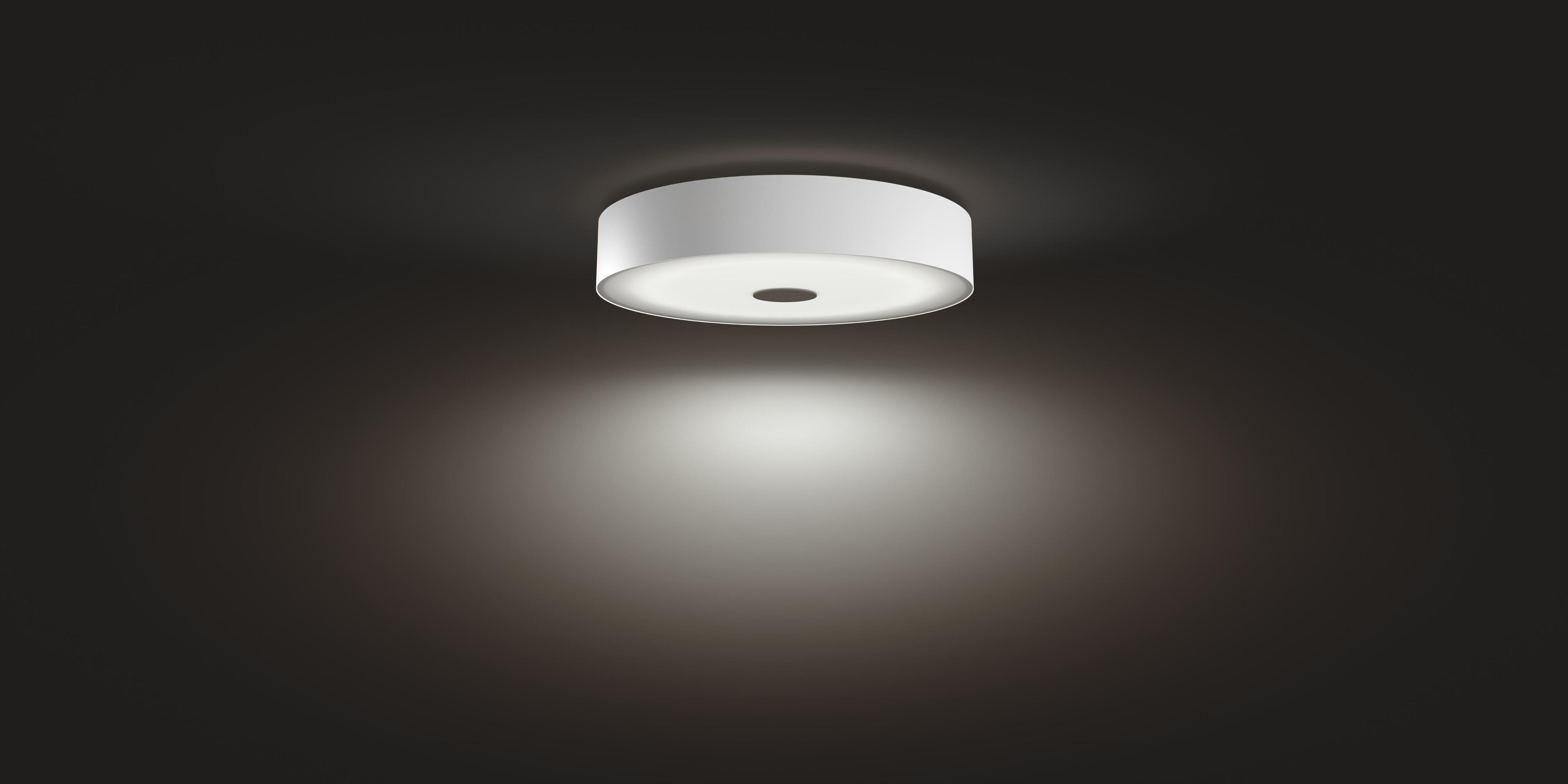 Un plafonnier circulaire blanc, projetant une lueur douce sur un fond gris foncé.