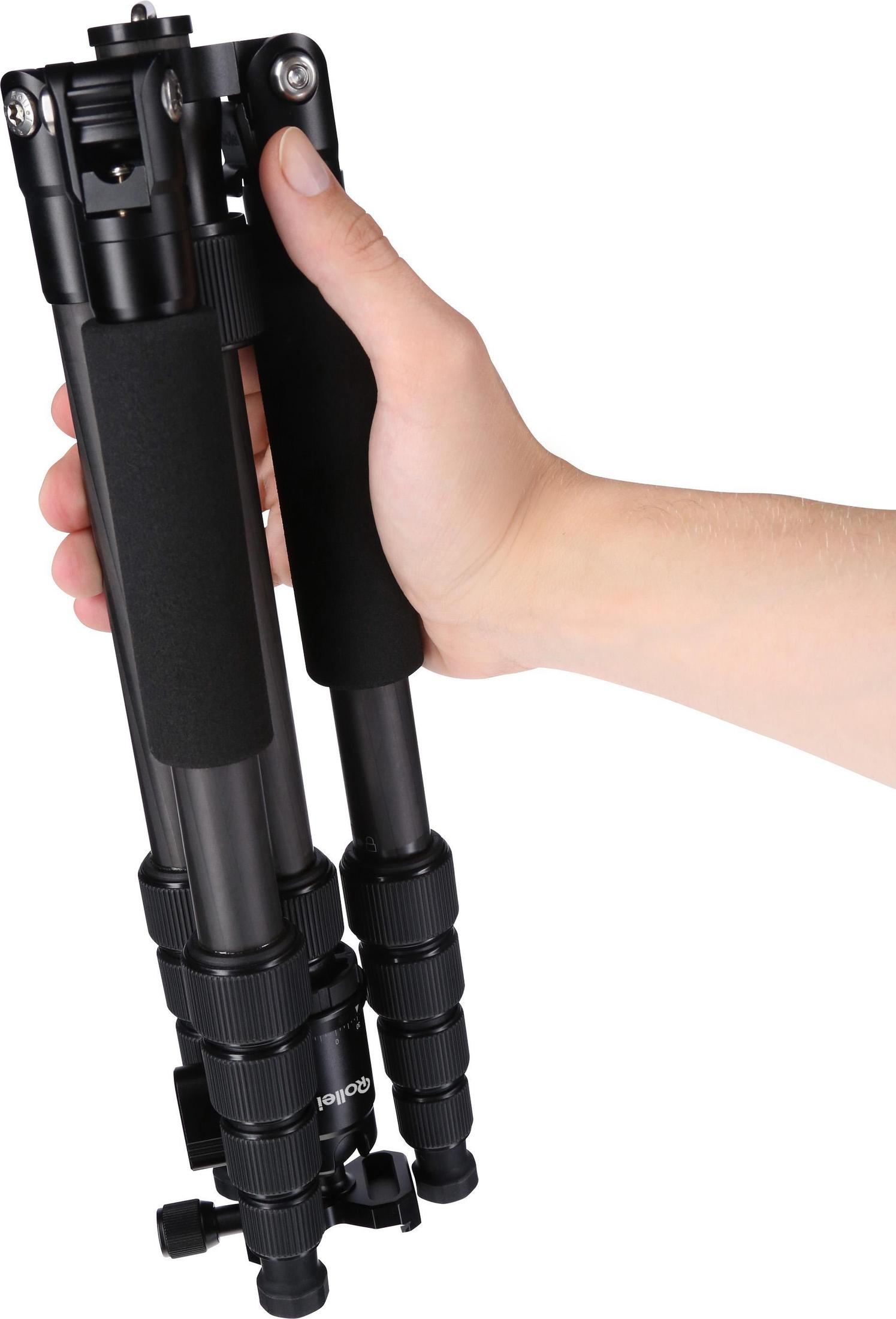 Dłoń trzyma złożony czarny statyw. Statyw ma piankowe uchwyty. Tło jest białe.