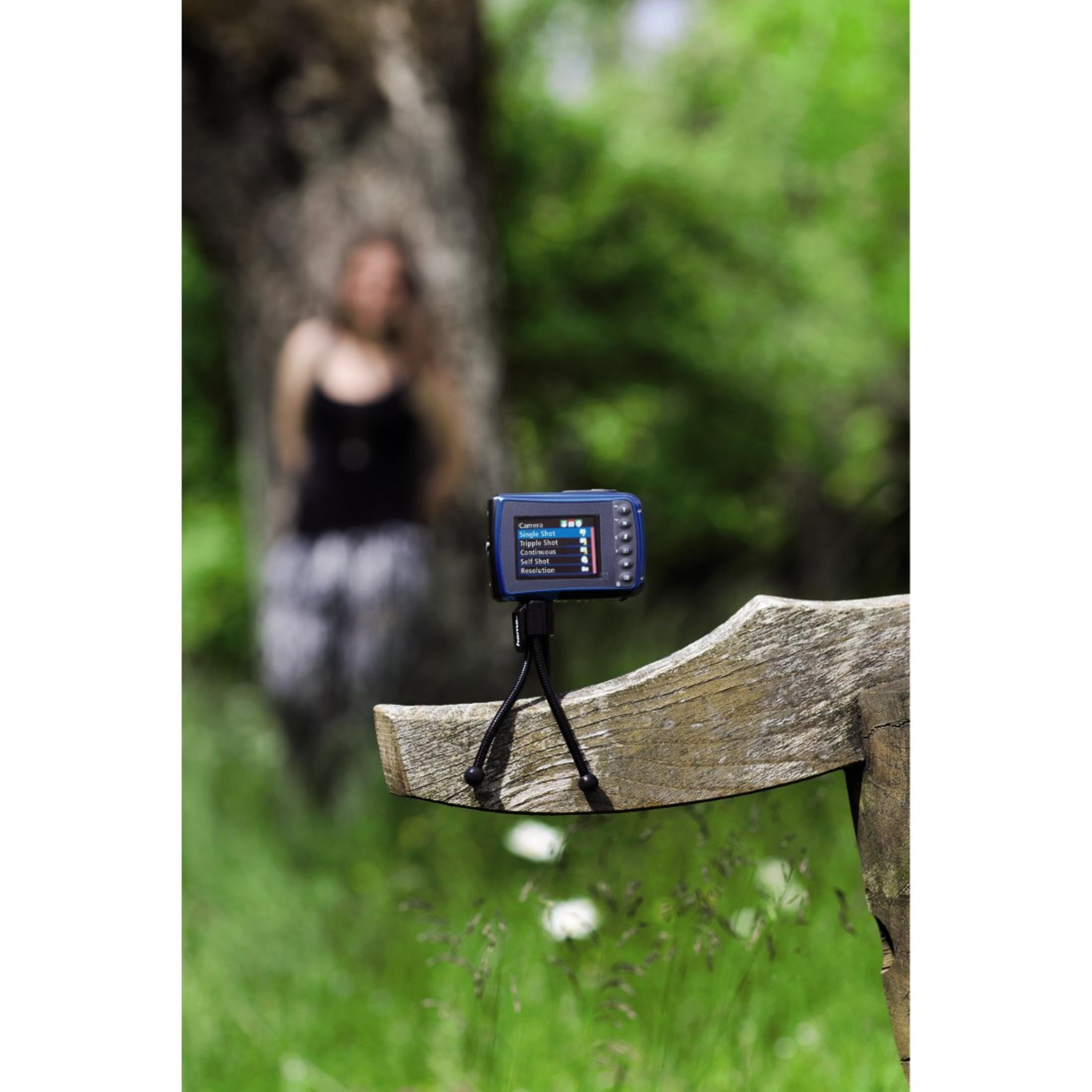 Una cámara digital en un trípode sobre una valla de madera. Una mujer borrosa está en el fondo.