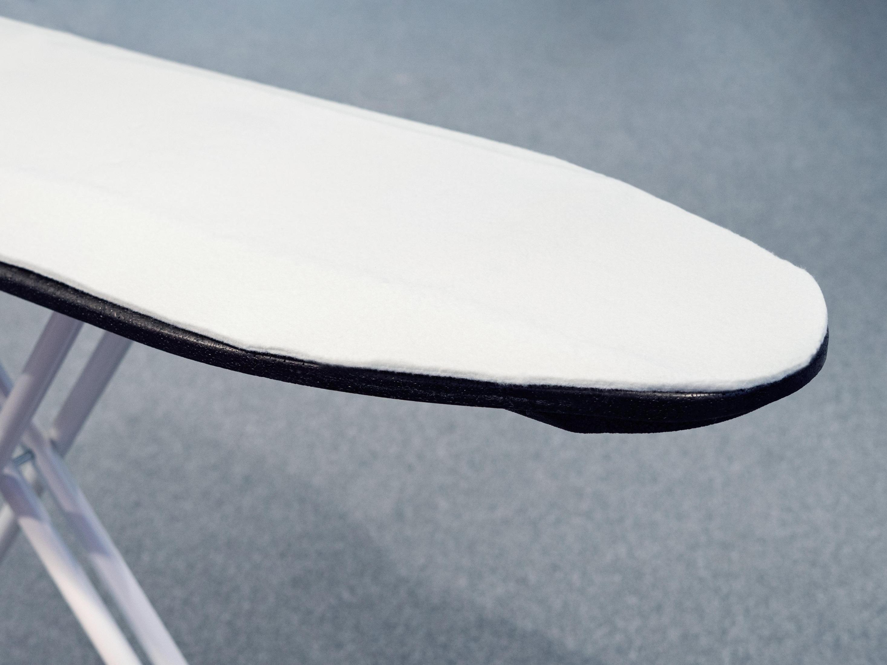 Zbliżenie na powierzchnię deski do prasowania, białą z czarną krawędzią, białe nogi.