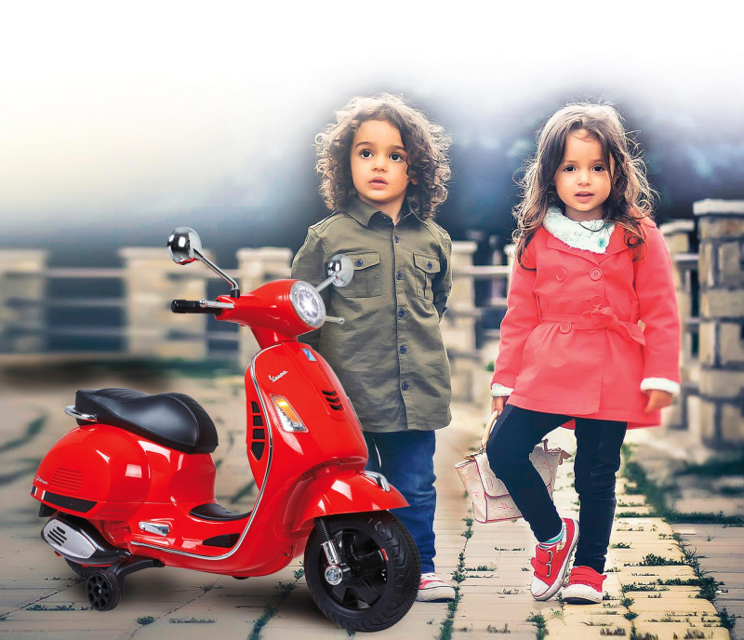 Dos niños con un scooter Vespa rojo. El fondo es una escena borrosa al aire libre.