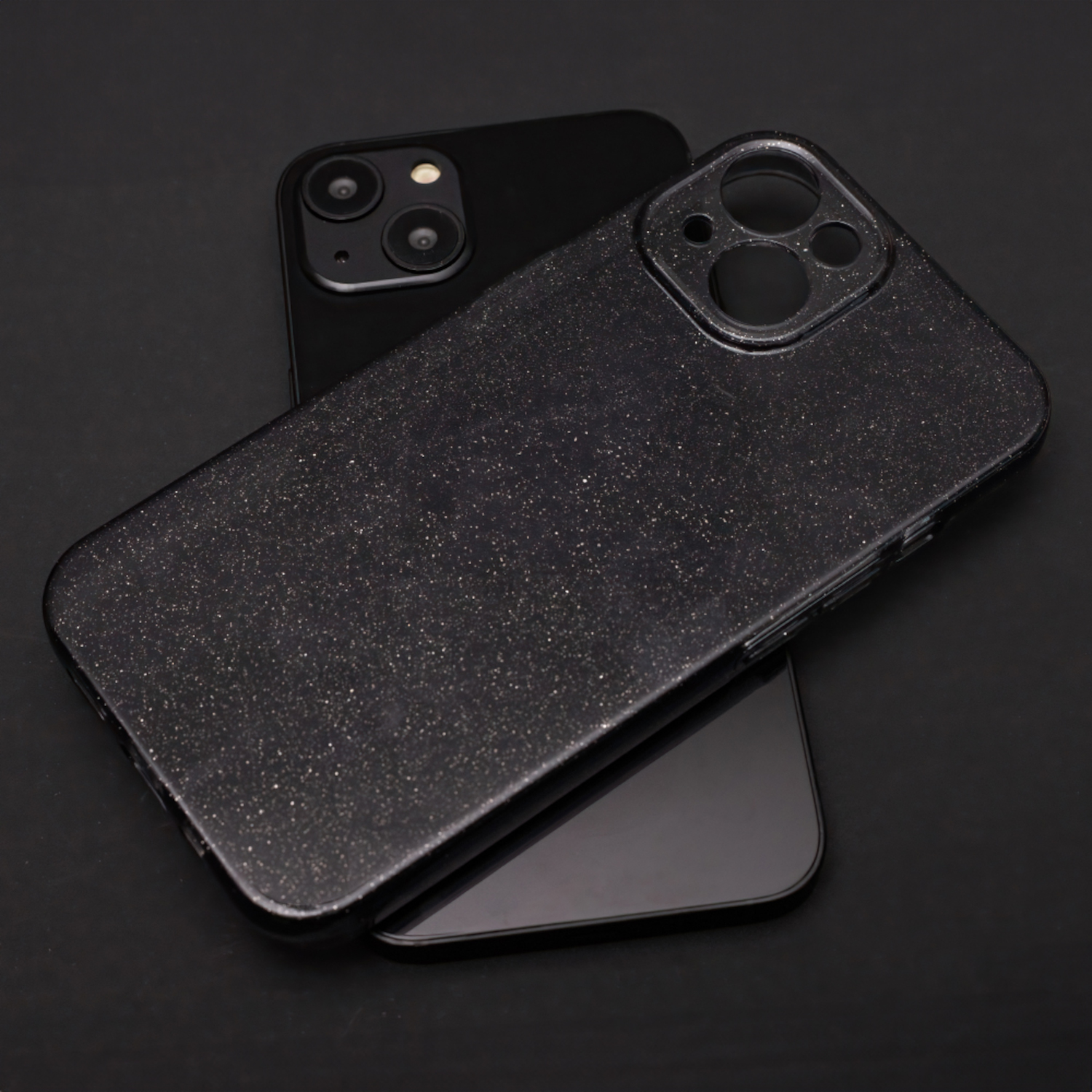 Zwei schwarze Telefone, eines mit glitzerndem Gehäuse, auf einer schwarzen Oberfläche gestapelt.