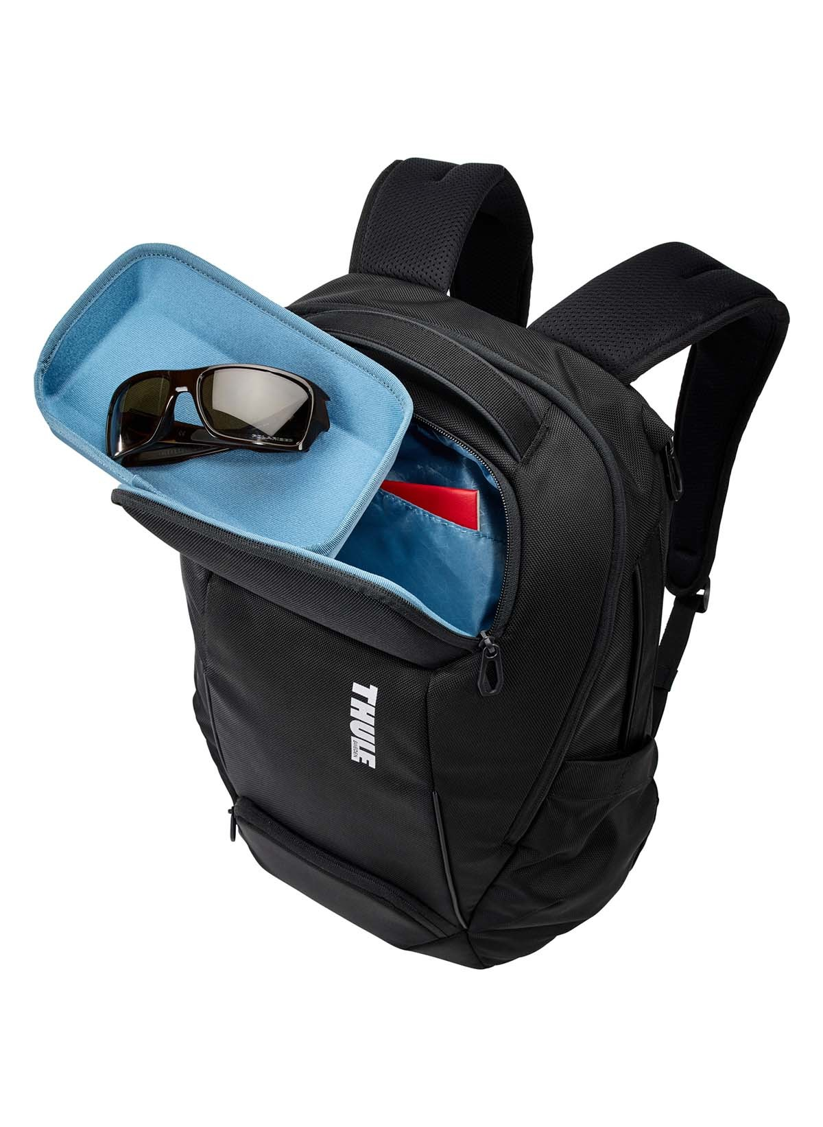 Ein schwarzer Thule-Rucksack, teilweise geöffnet, mit einem blauen Etui mit Sonnenbrille und einem roten Notizbuch darin.