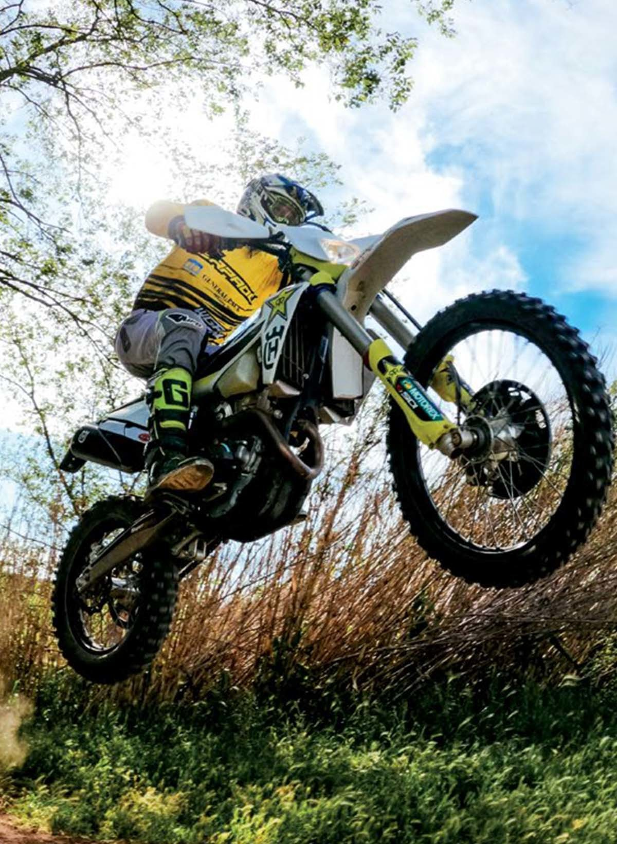 Une personne sur une moto de motocross sautant en l'air, avec un fond de ciel bleu.