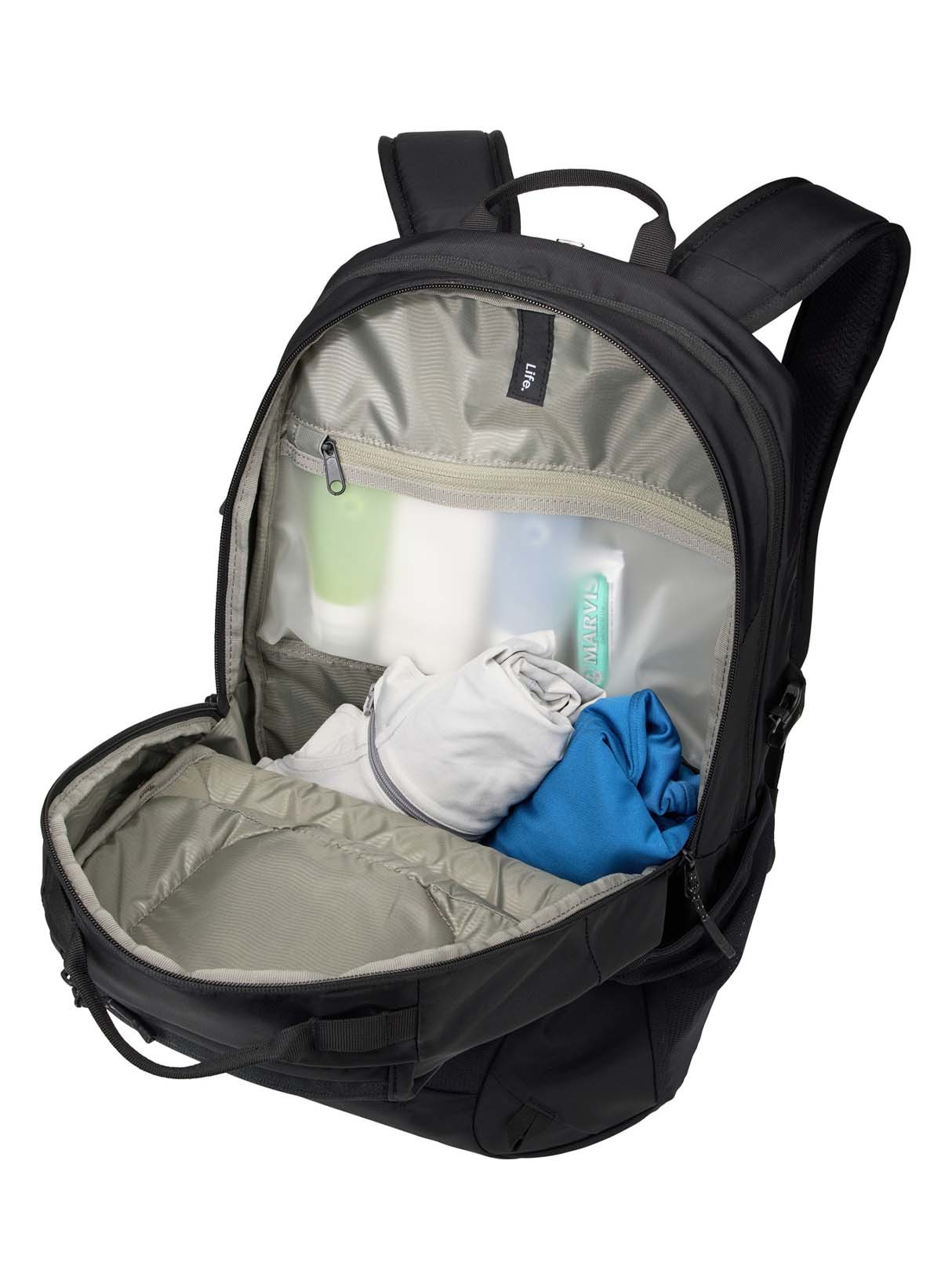 Una mochila negra abierta con objetos dentro, incluyendo ropa y artículos de aseo.
