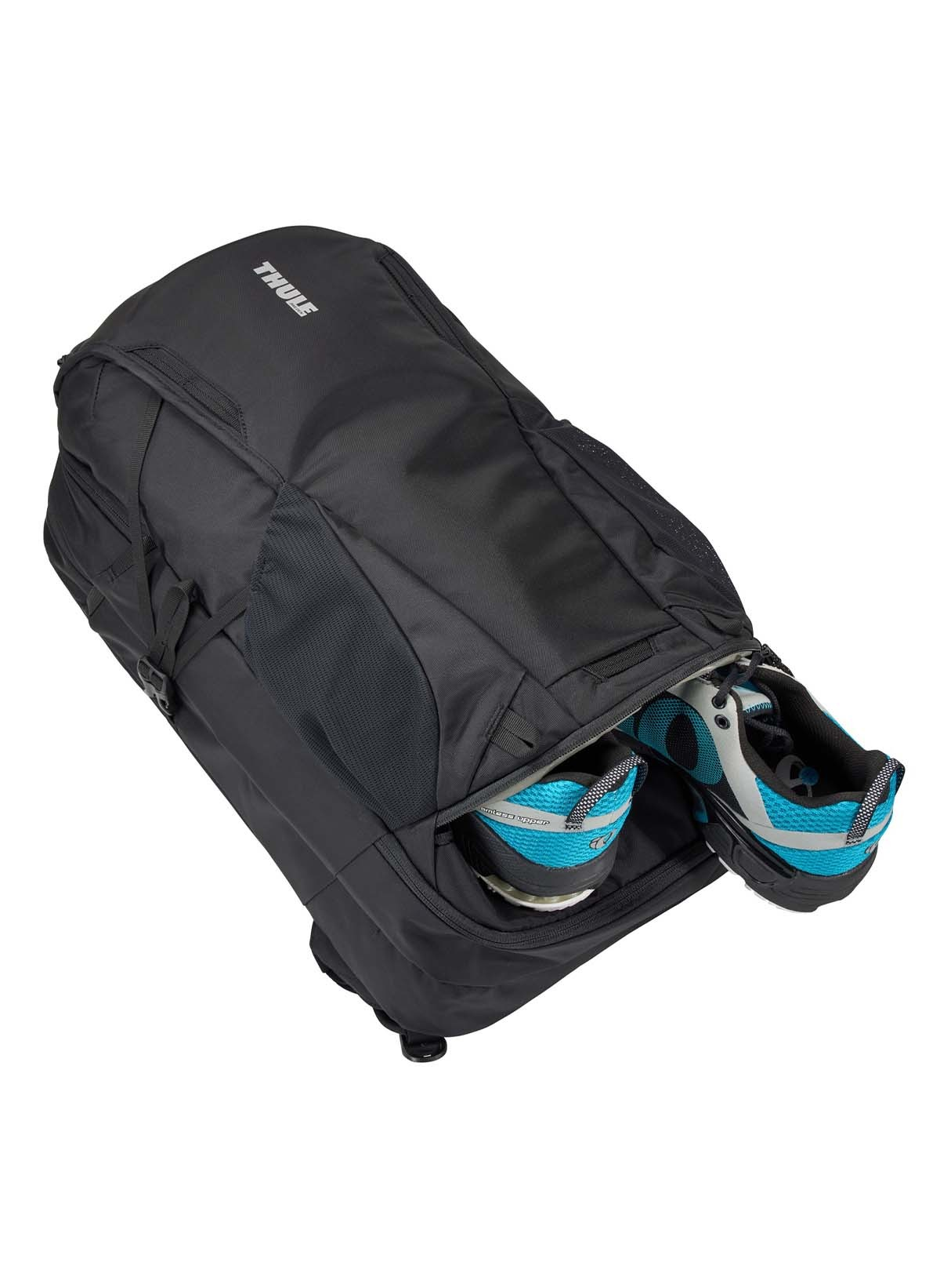 Eine schwarze Reisetasche mit zwei blauen und grauen Schuhen, die von der Seite sichtbar sind, vor weißem Hintergrund.