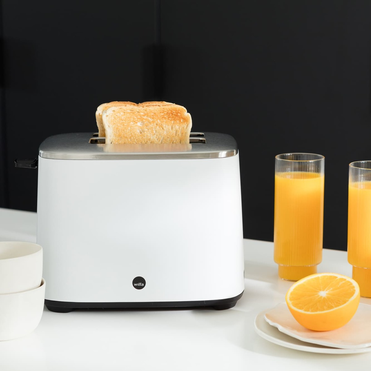 Ein weißer Toaster mit zwei Toastscheiben, Orangensaft und einem weißen Tisch.