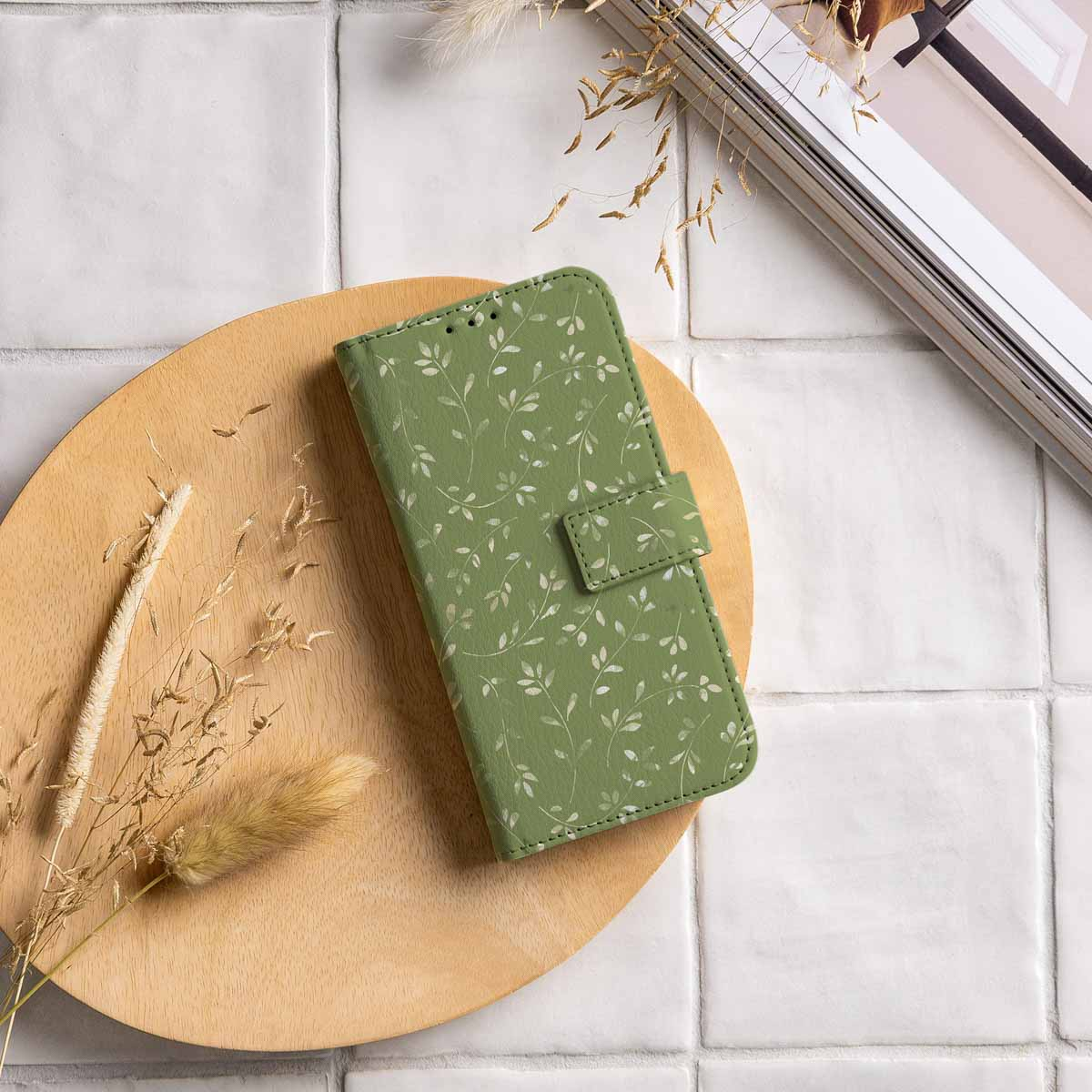 Een groene bloemen telefoonhoes ligt op een houten dienblad met droogbloemen.