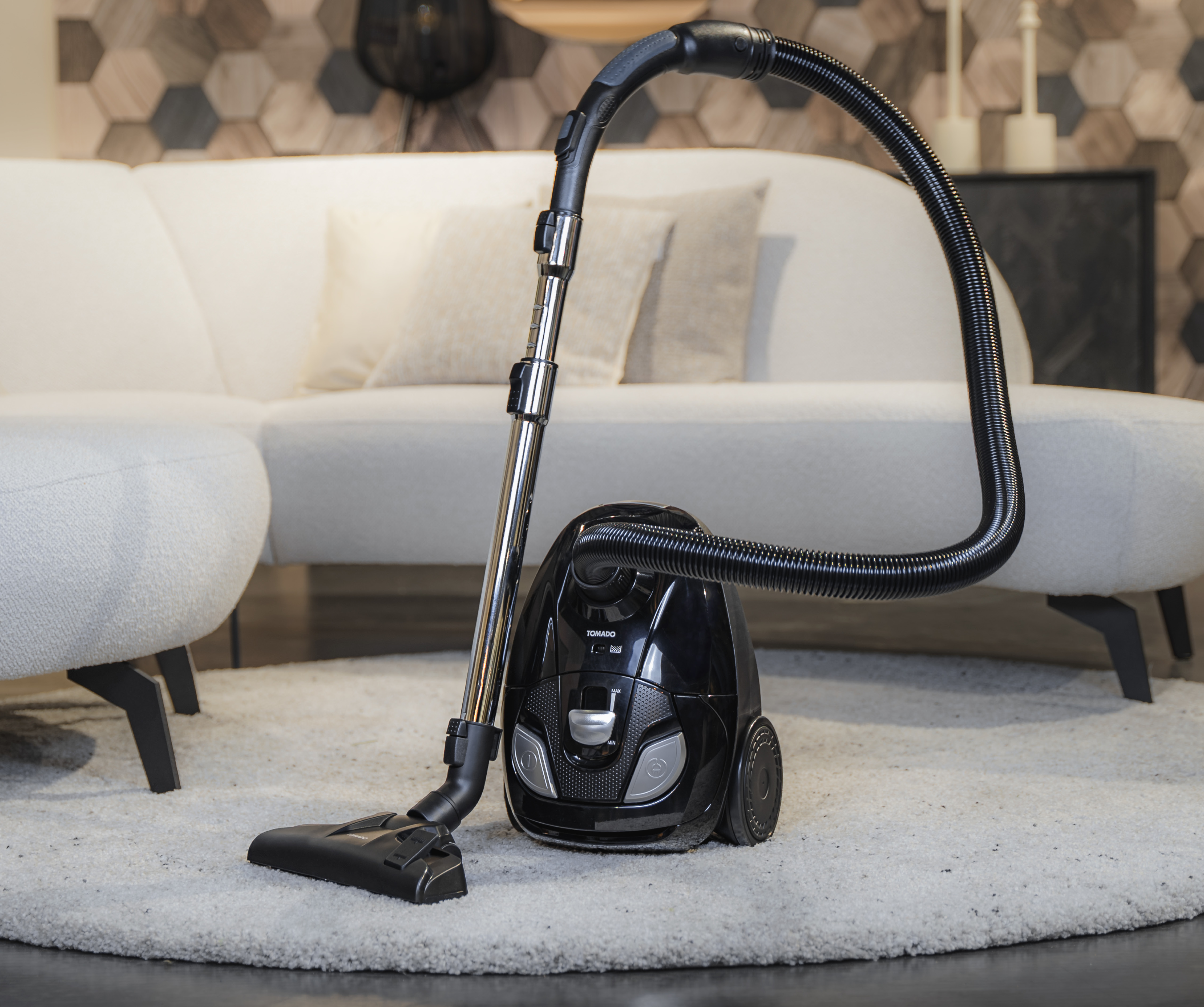 Black and silver vacuum cleaner on a patterned rug in a living room setting, with a white couch.