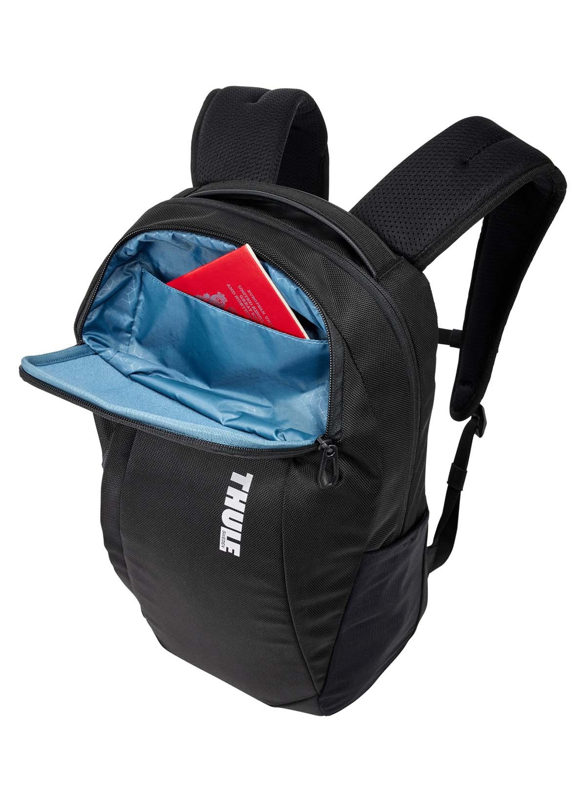 Ein schwarzer Thule-Rucksack mit offener Vordertasche, die einen roten Reisepass zeigt. Weißer Hintergrund.