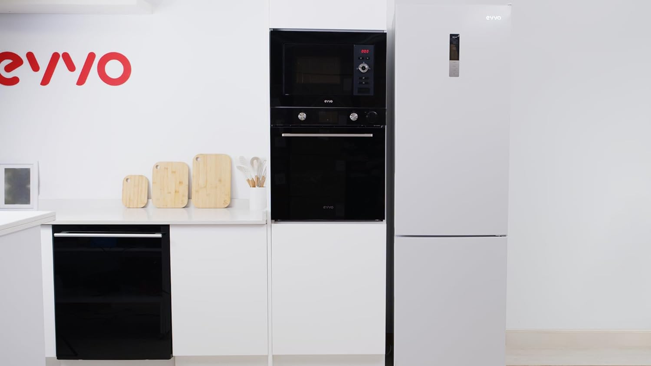 Cocina blanca con nevera, microondas, horno y tablas de cortar blancos.