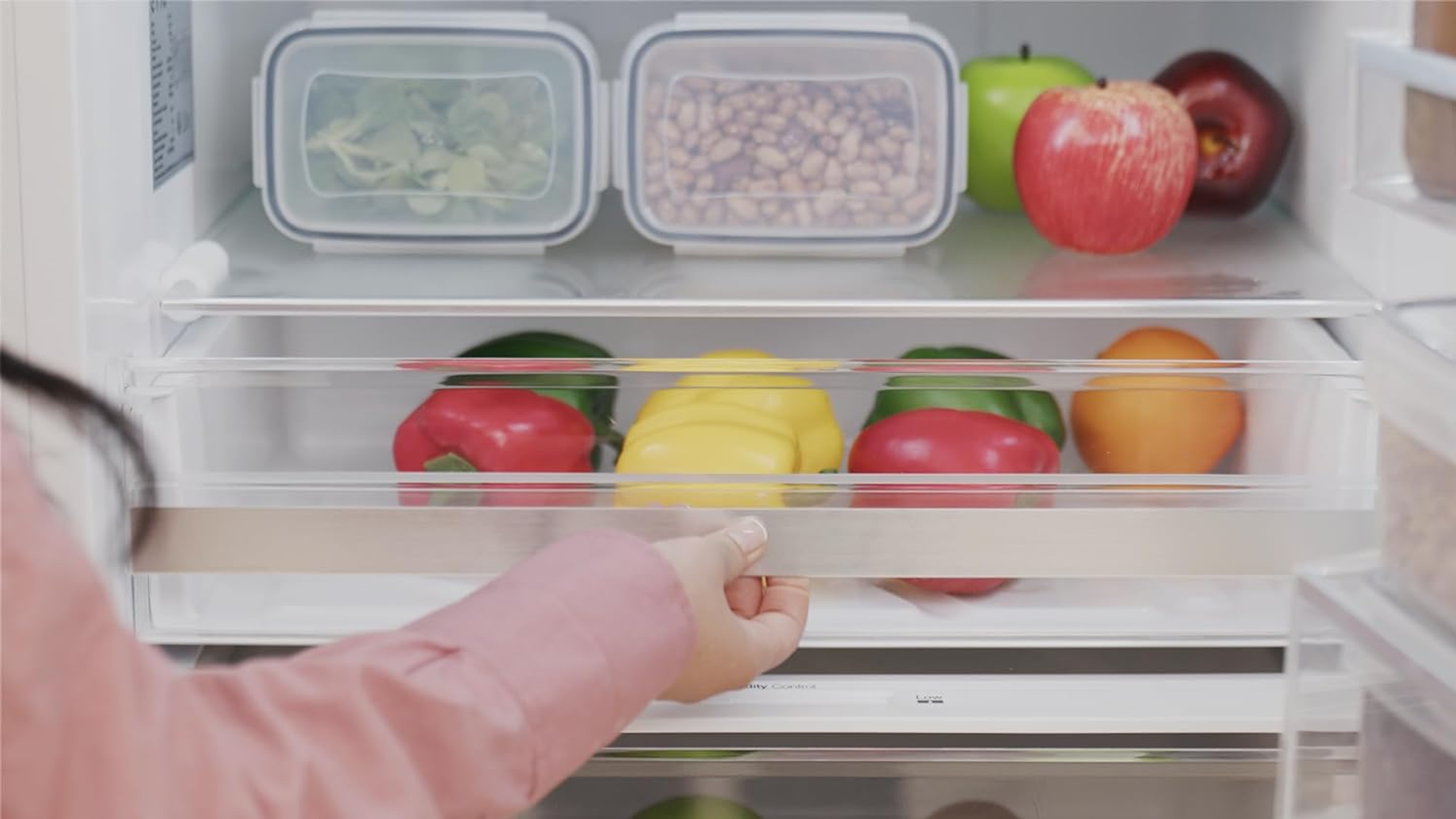 Un refrigerador con un cajón abierto, que muestra pimientos rojos, amarillos y manzanas arriba.
