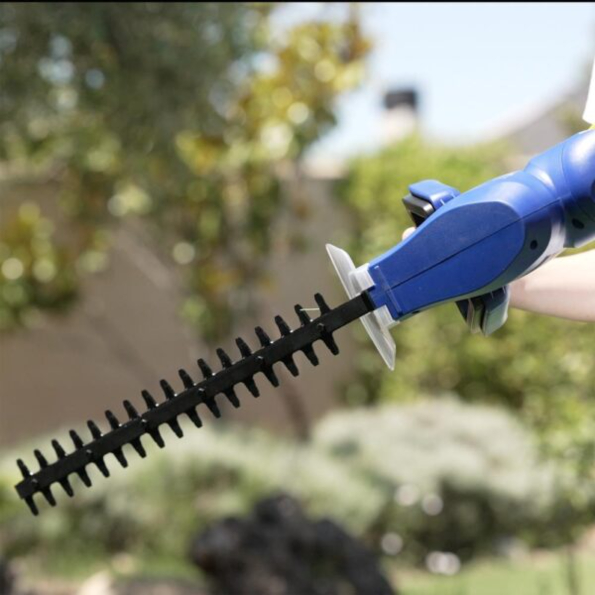 Un cortasetos azul y negro que se utiliza al aire libre entre vegetación.