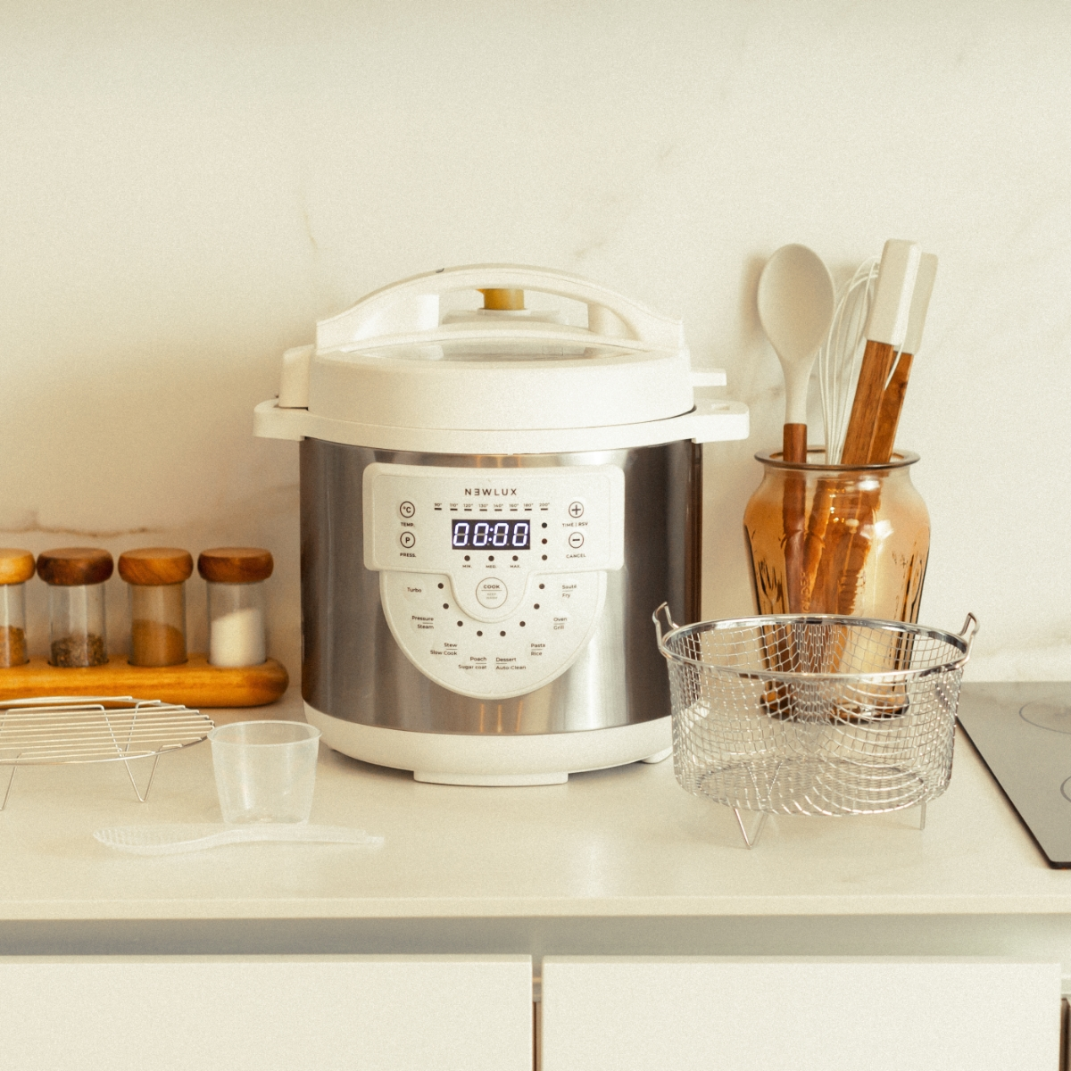Olla a presión de acero inoxidable y plata con pantalla digital, junto a utensilios de cocina e ingredientes.
