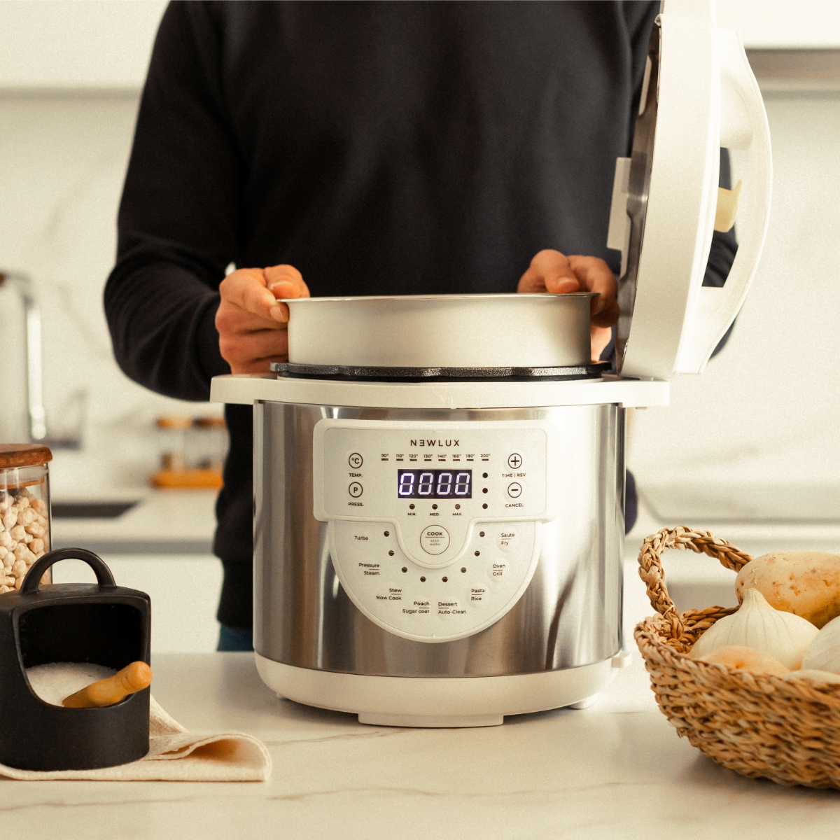 Una persona está poniendo una sartén en una olla a presión. Encimera, ingredientes y un cuenco negro están presentes.