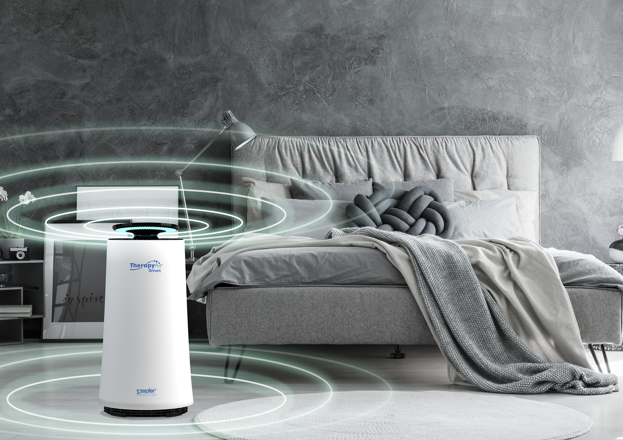 Weißer Luftreiniger in einem Schlafzimmer, mit Bett, Lampe und Bilderrahmen.