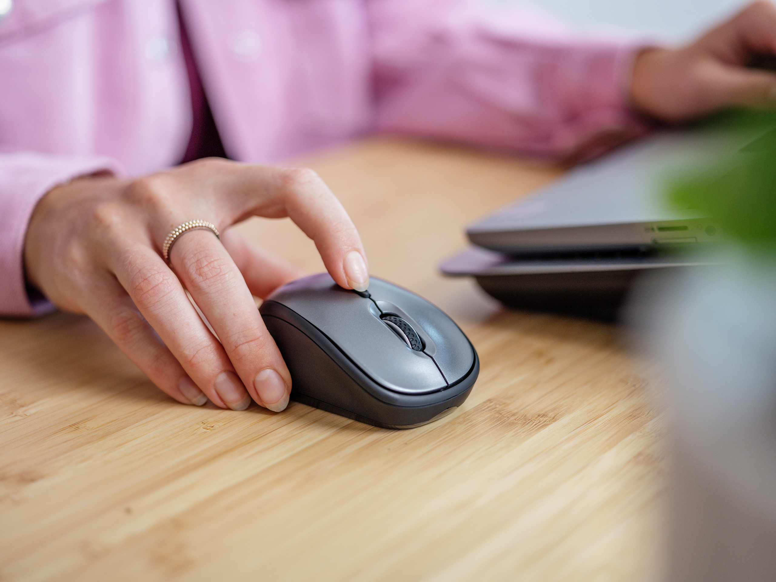 Dłoń osoby używającej szarej myszy komputerowej na drewnianym biurku.